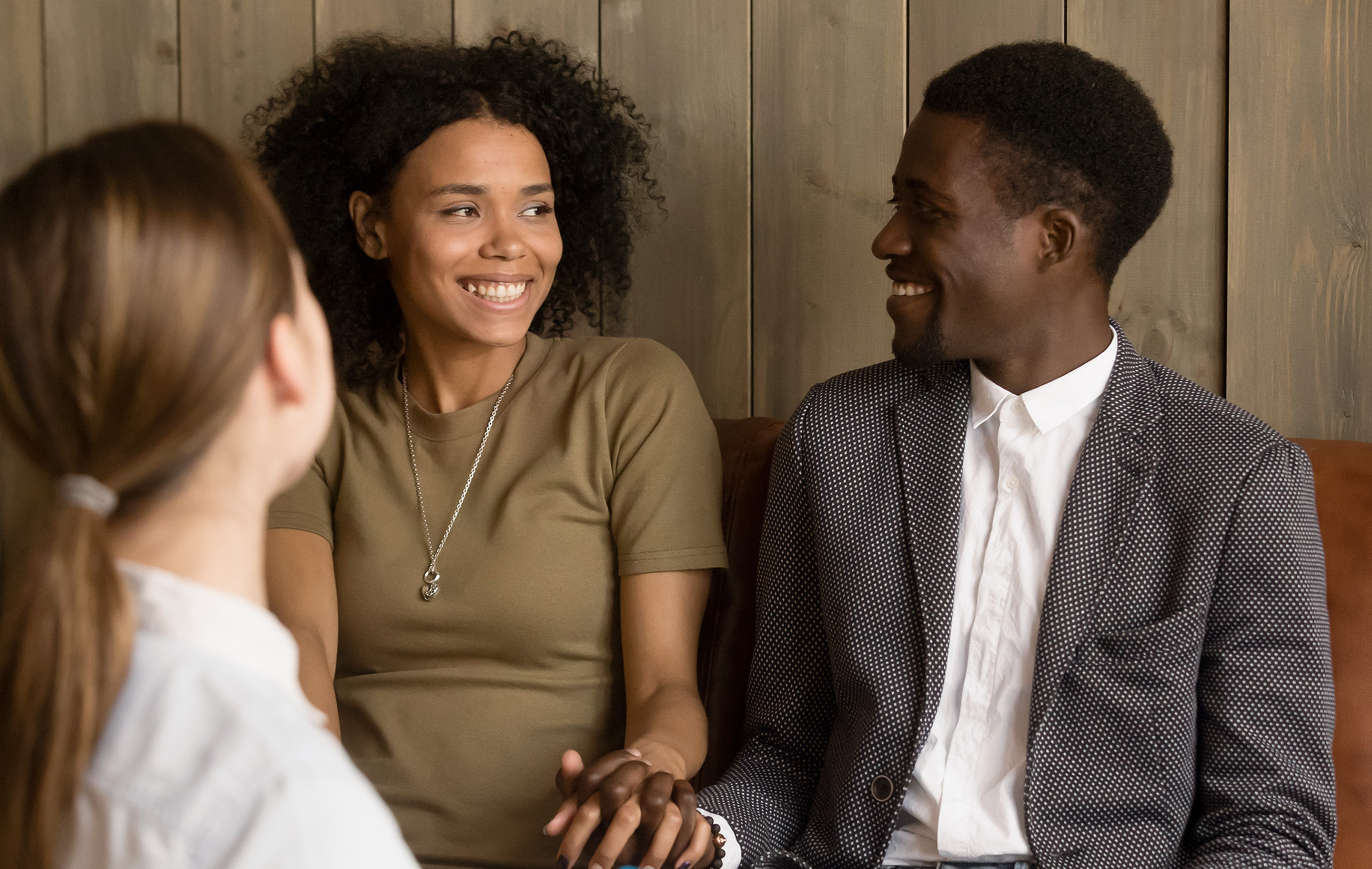 Three friends laugh and smile in a warm, wooden room, sharing a joyful conversation.