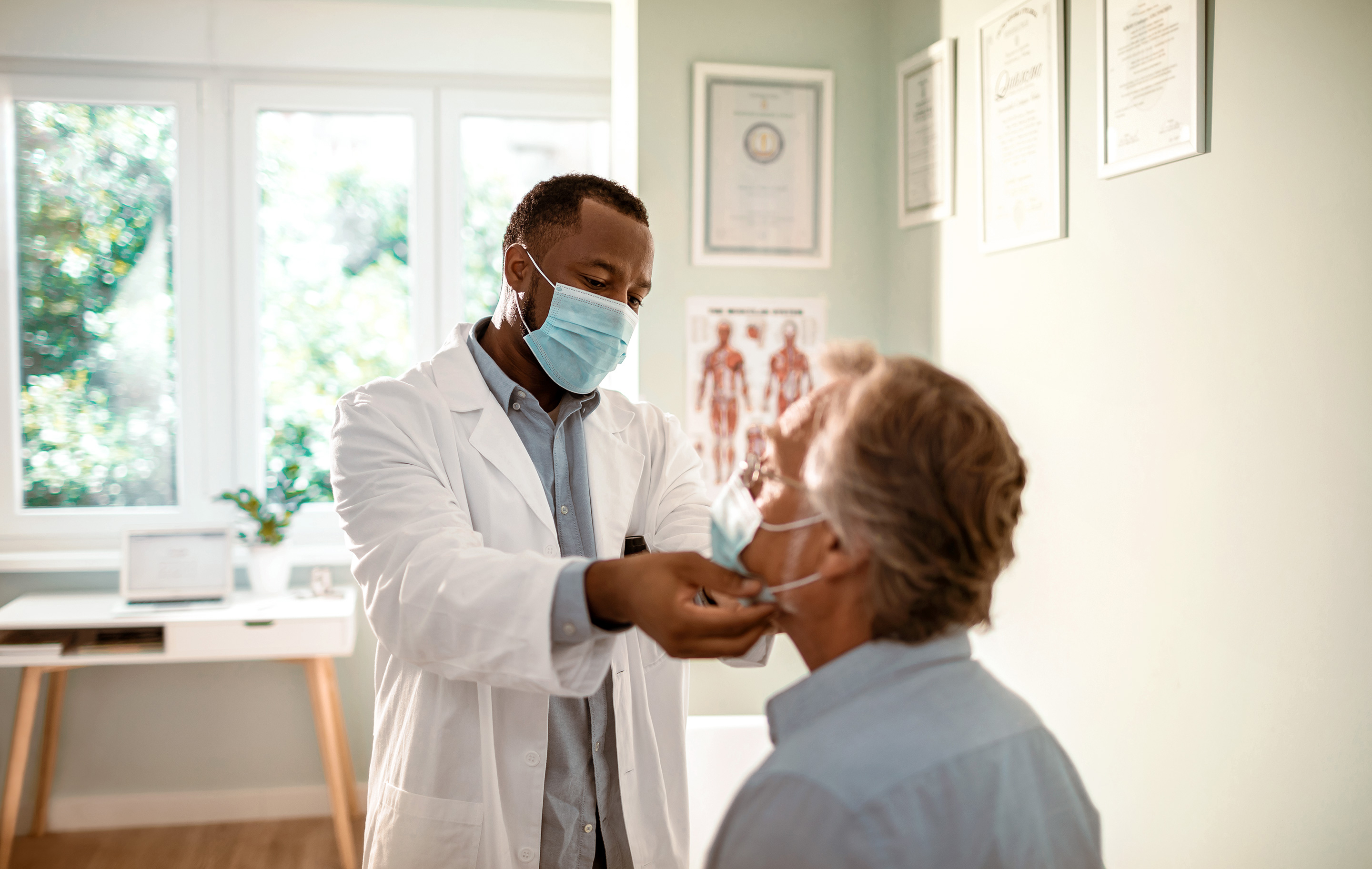 Doctor wearing mask examines patient in bright, clinical office with natural light