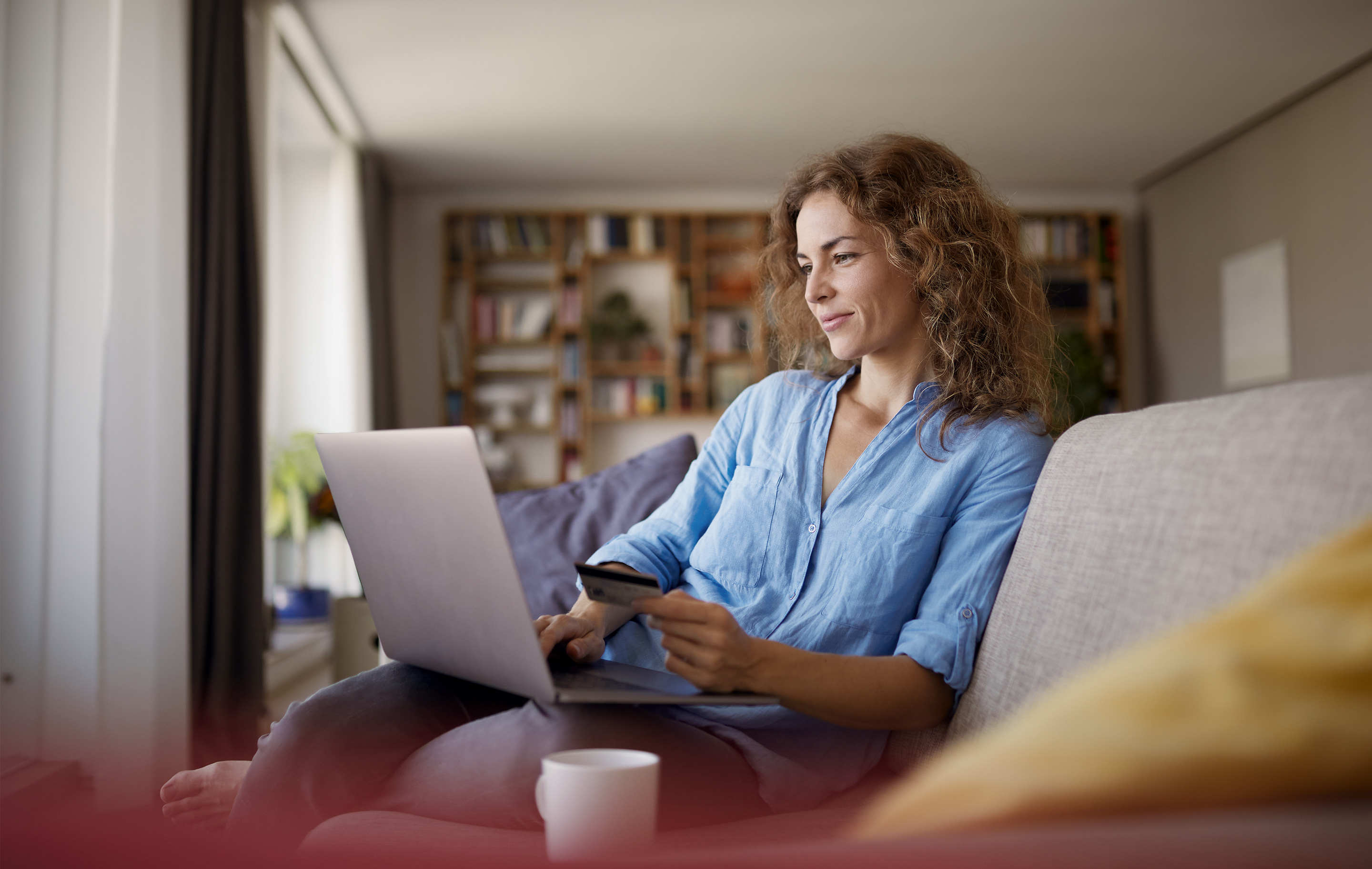 Woman in blue shirt sits on couch with laptop and coffee mug