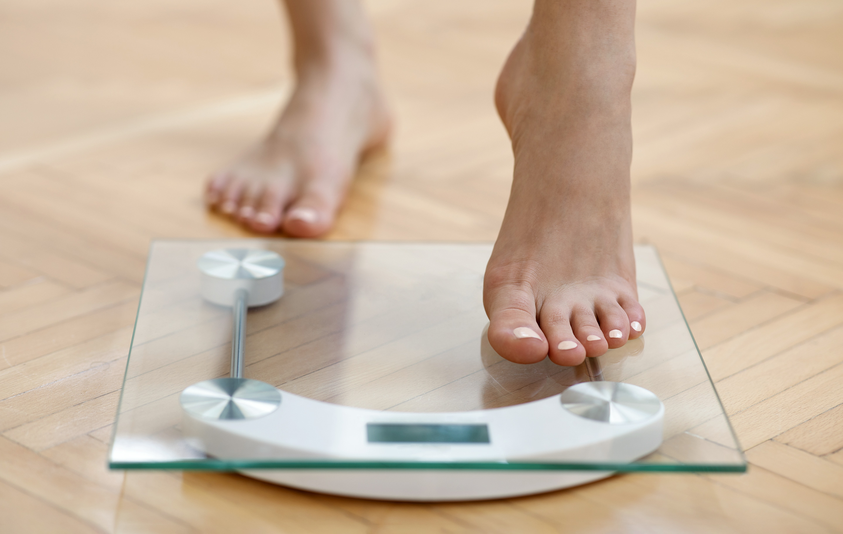 Bare feet stepping onto a modern glass digital scale on a wooden floor