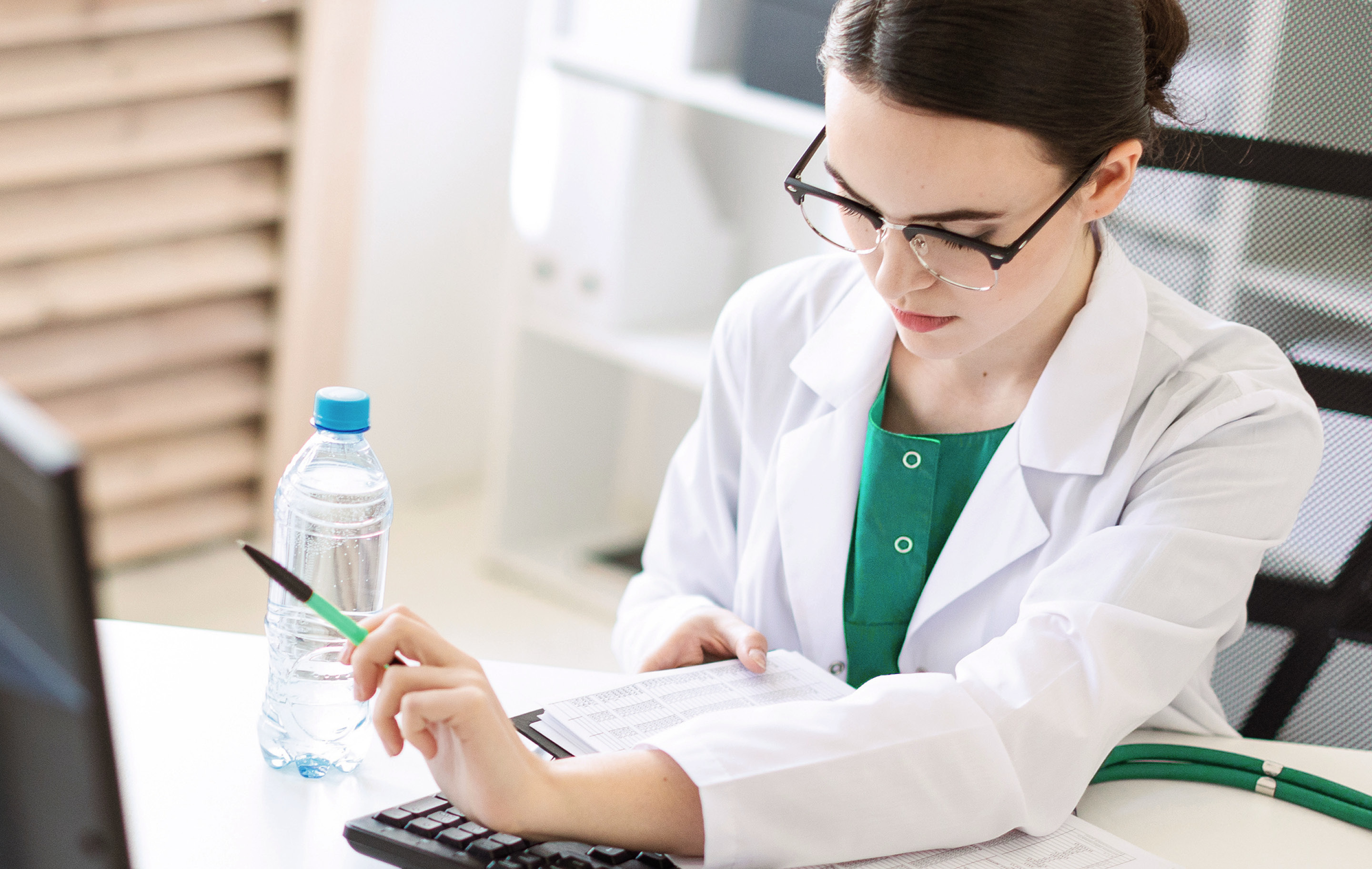 Female doctor in white coat and glasses reviews documents at desk