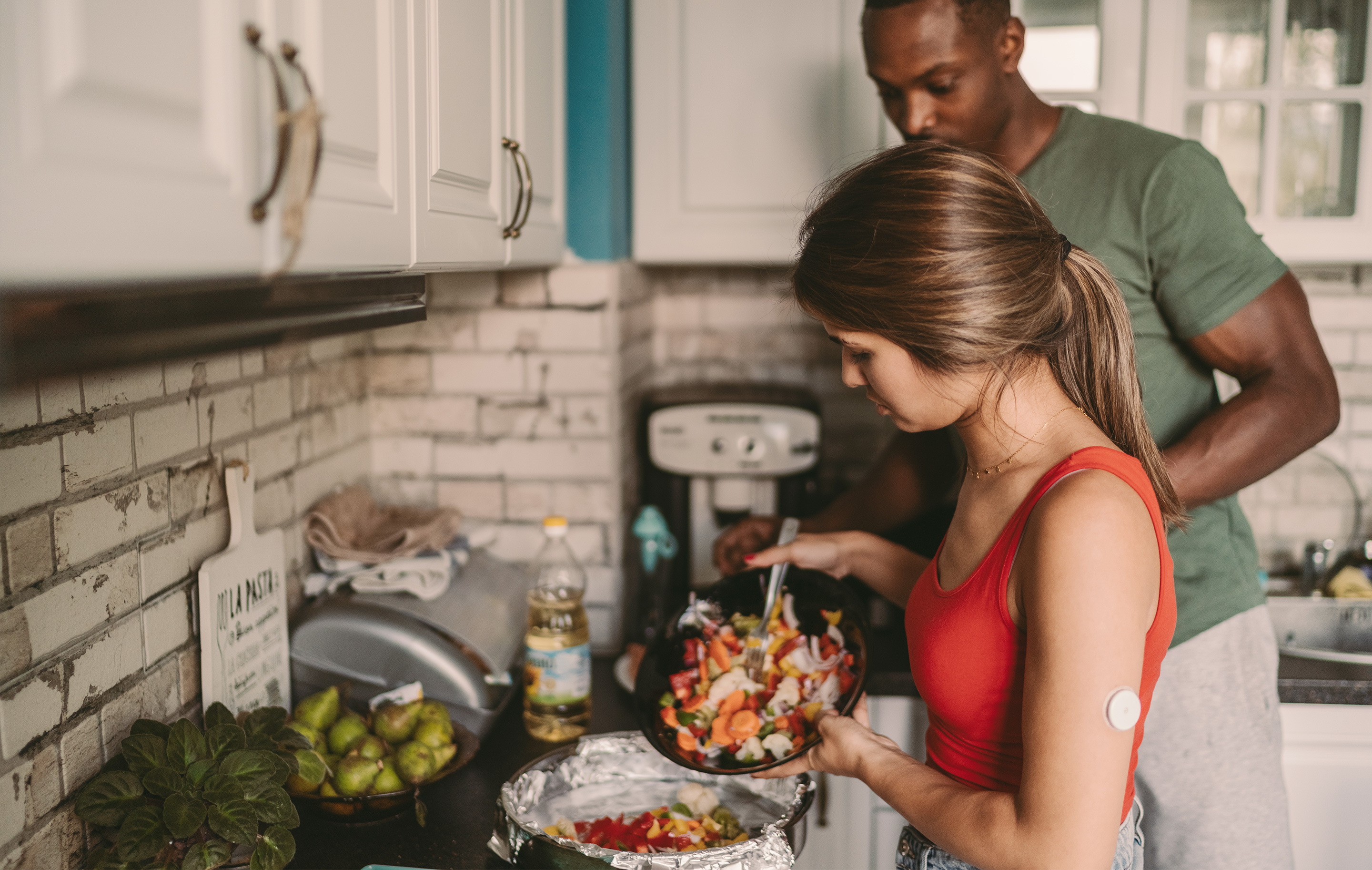 A man and woman in a kitchen preparing a meal together with a woman wearing a glucose monitor.