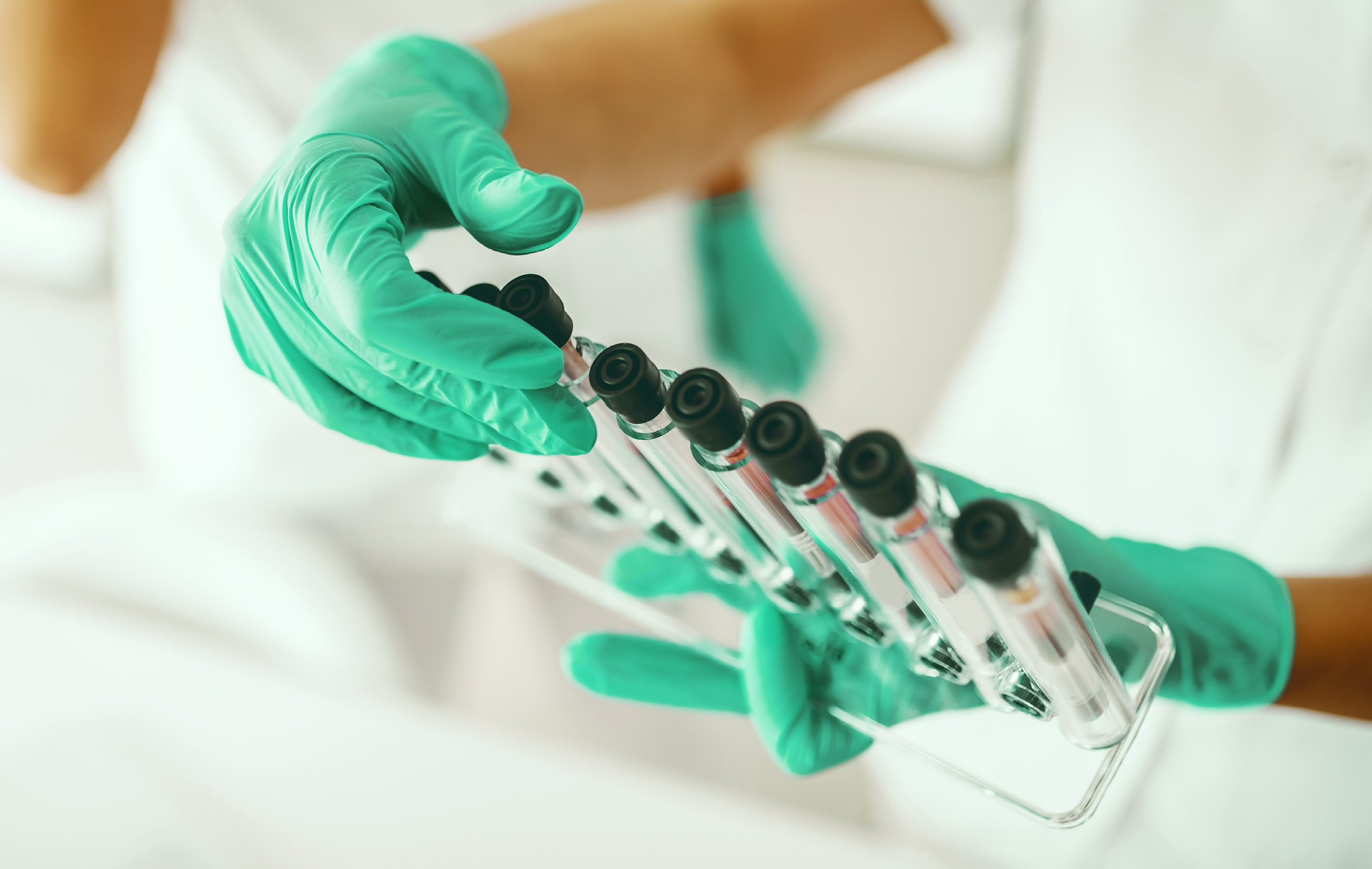 Scientist in green gloves holds test tubes in lab setting with sterile white background