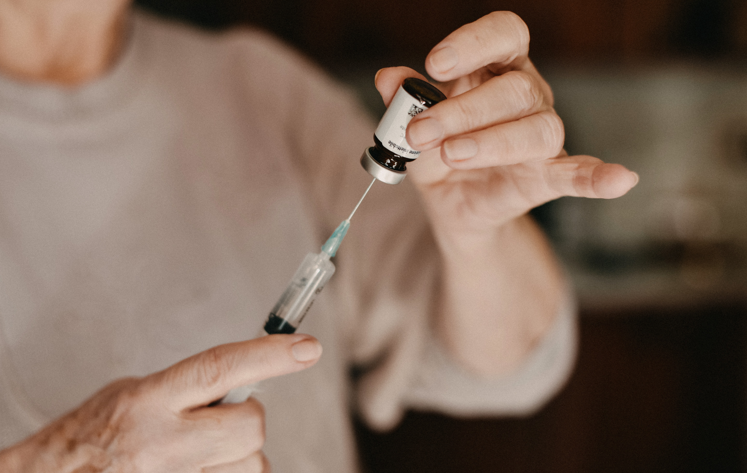Person holding syringe and vial in dimly lit room with neutral-toned clothing