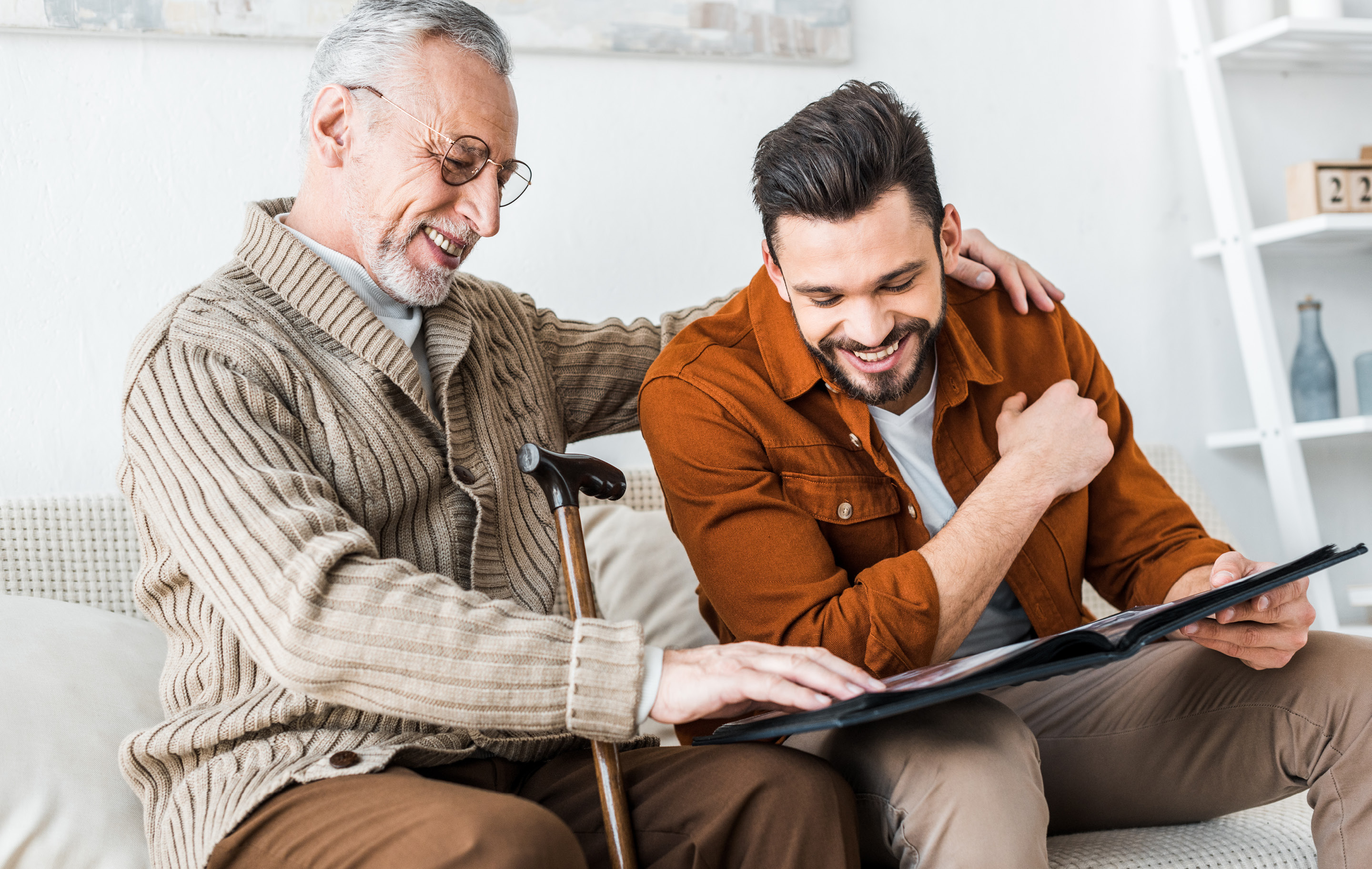 Two men share a joyful moment reviewing content on a tablet together in a bright, cozy living room setting