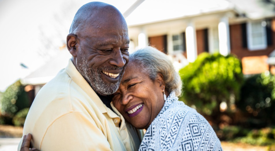 Smiling elderly couple embracing outside a home in warm sunlight