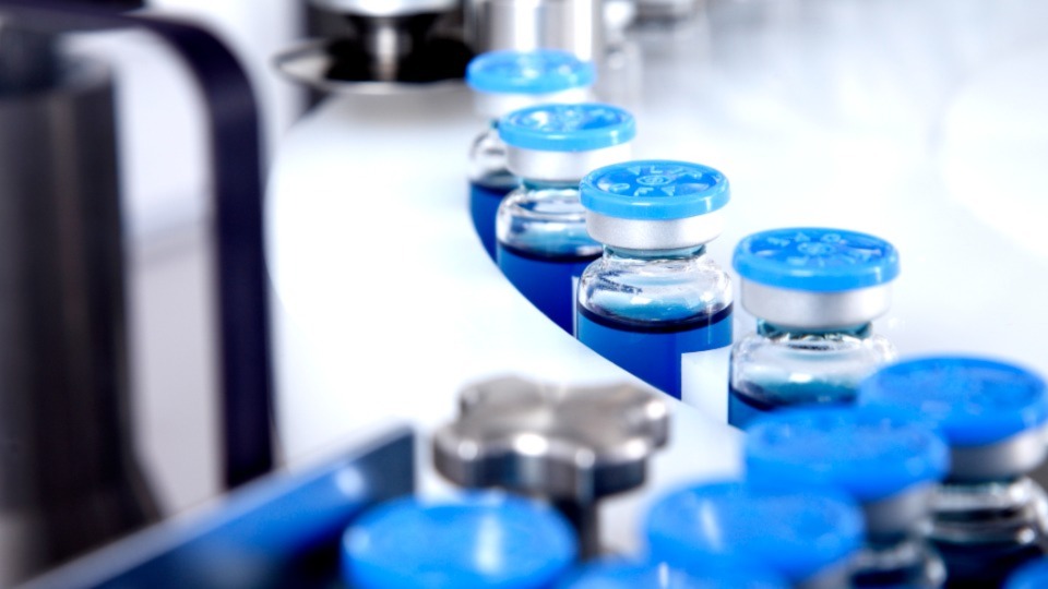 Blue-capped vials on a conveyor belt in a sterile pharmaceutical manufacturing facility