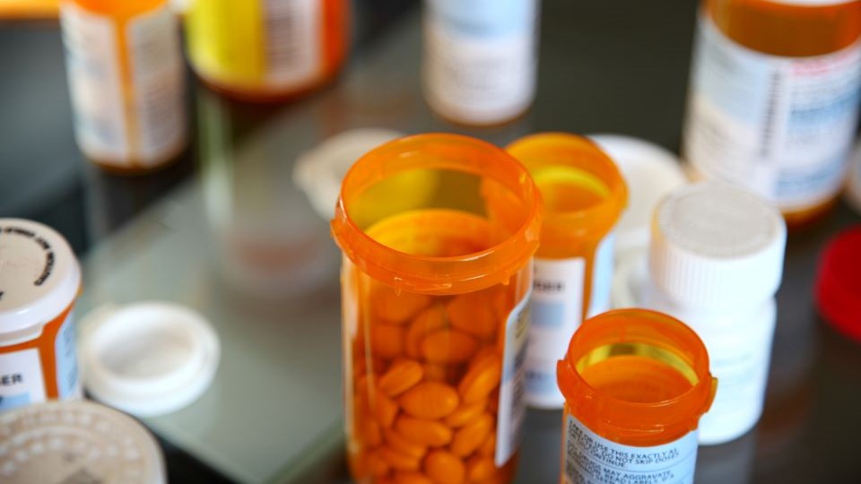 Multiple prescription bottles on a dark surface with one open, revealing pills inside