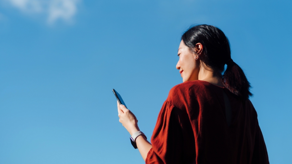 Woman in red sweater outdoors under clear blue sky, smiling while looking at phone