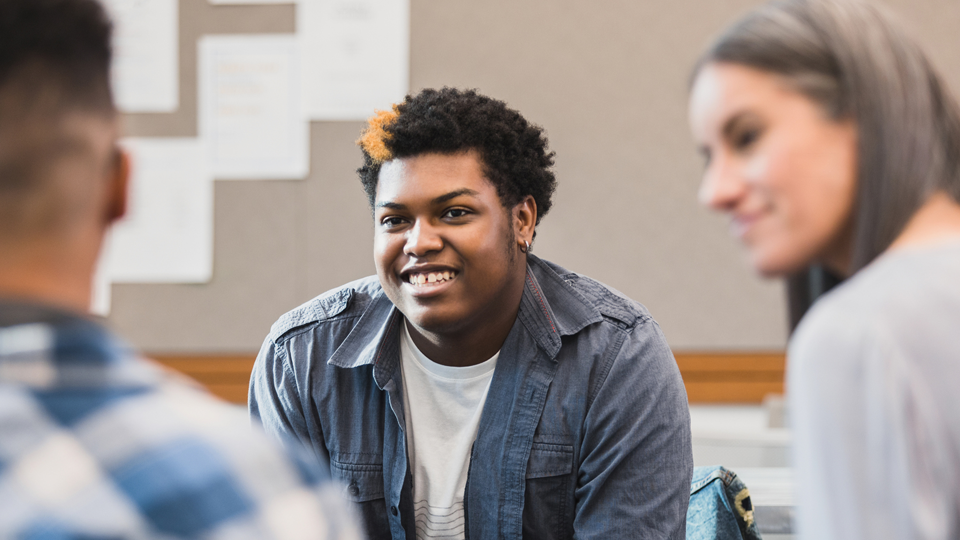 Three people smiling and chatting in a classroom setting
