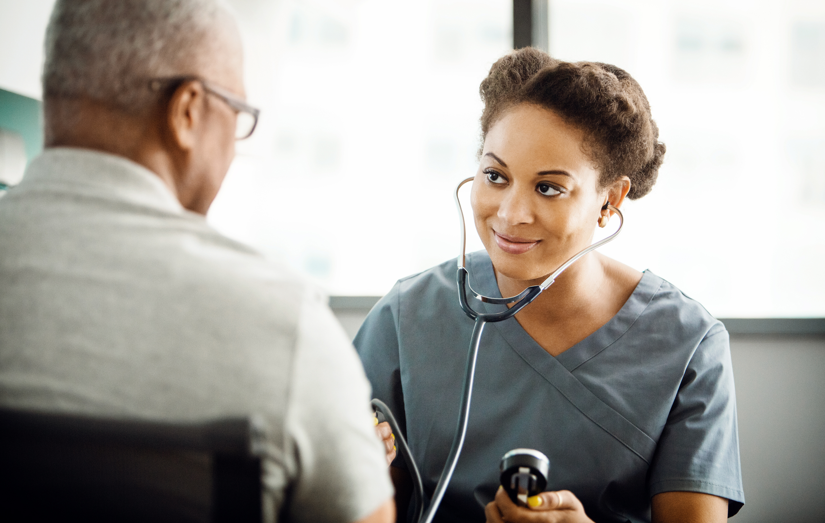 Healthcare provider uses stethoscope and blood pressure monitor with patient in clinical setting.