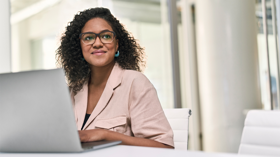 Smiling woman with glasses working on laptop in modern office setting