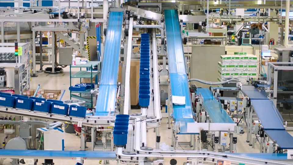Industrial conveyor system with blue belts transporting blue bins through a complex automated manufacturing setup.