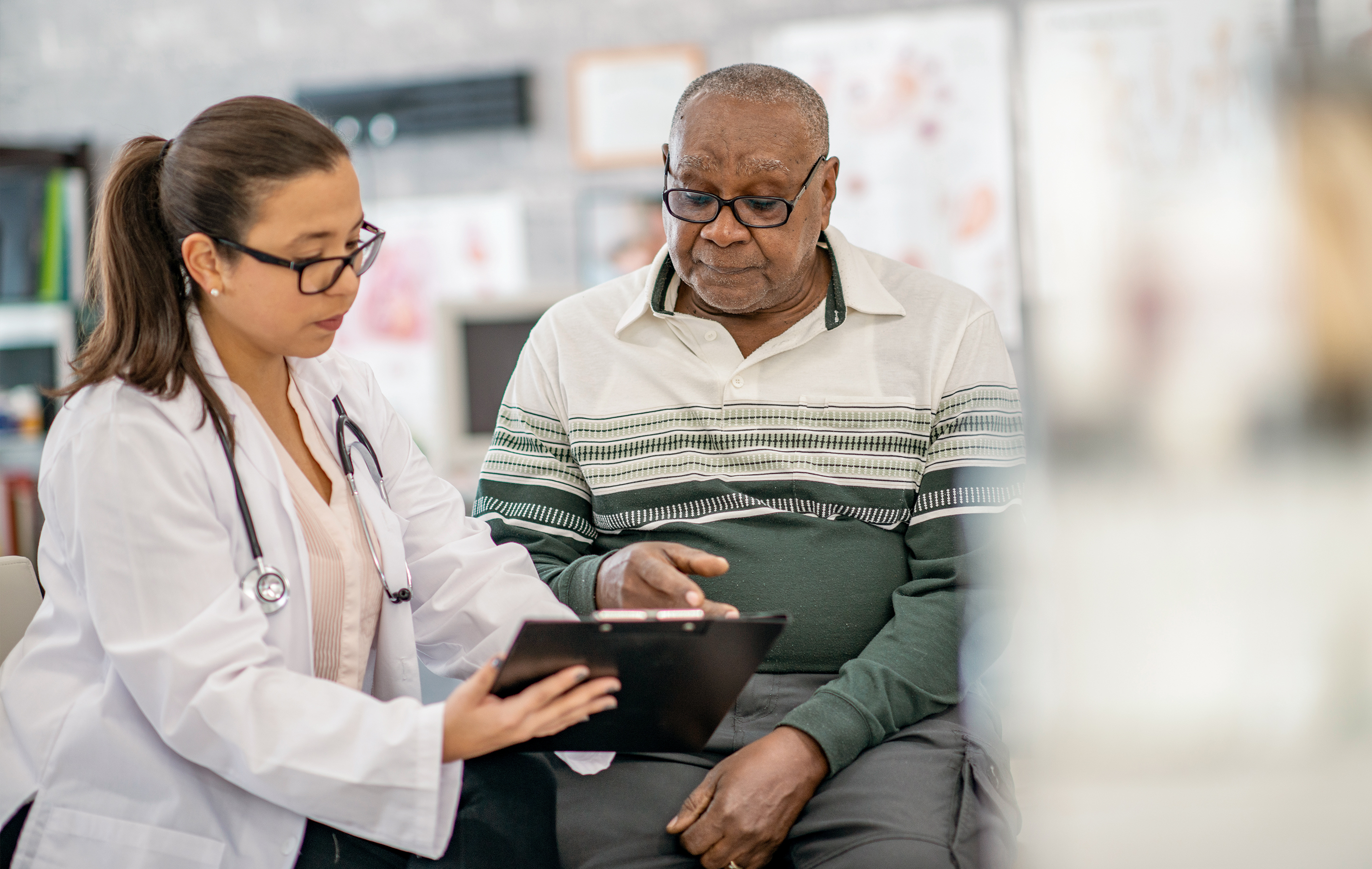 Doctor using tablet with elderly patient in clinical setting, focused on health consultation.
