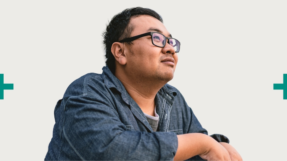 Man in glasses and denim jacket looks thoughtfully upward