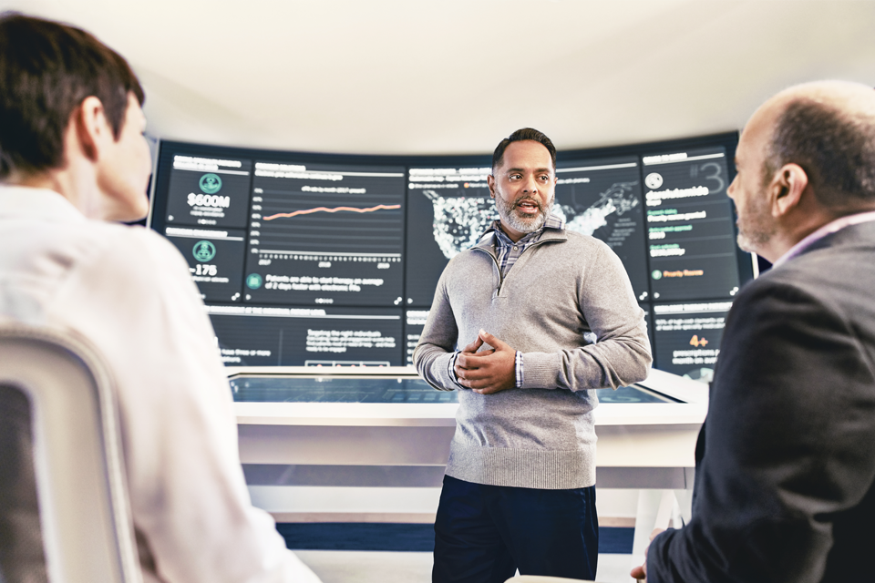 Man presenting data on large screen to male and female in office
