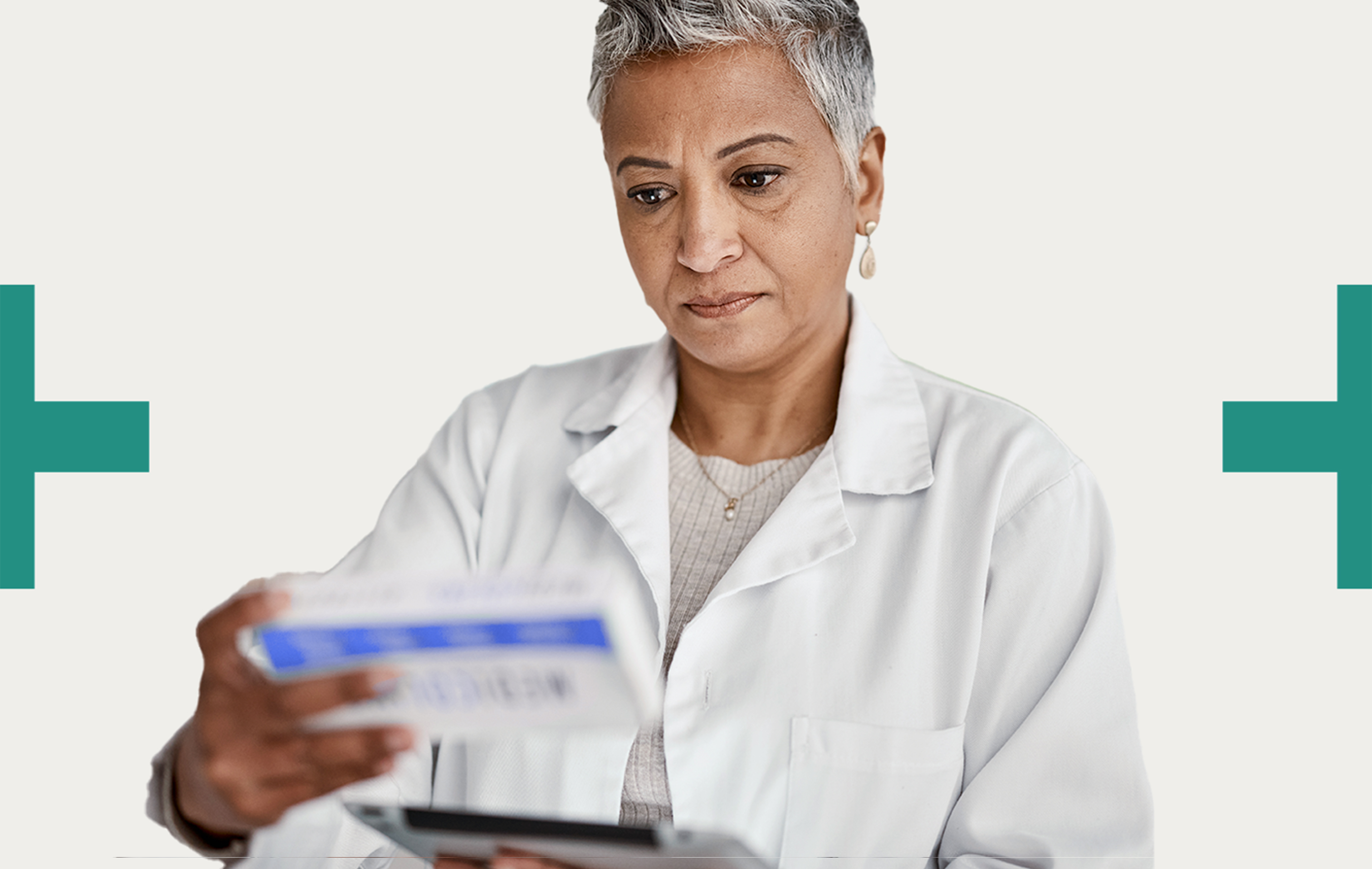 A healthcare professional in a white coat reviews a prescription while holding a tablet.