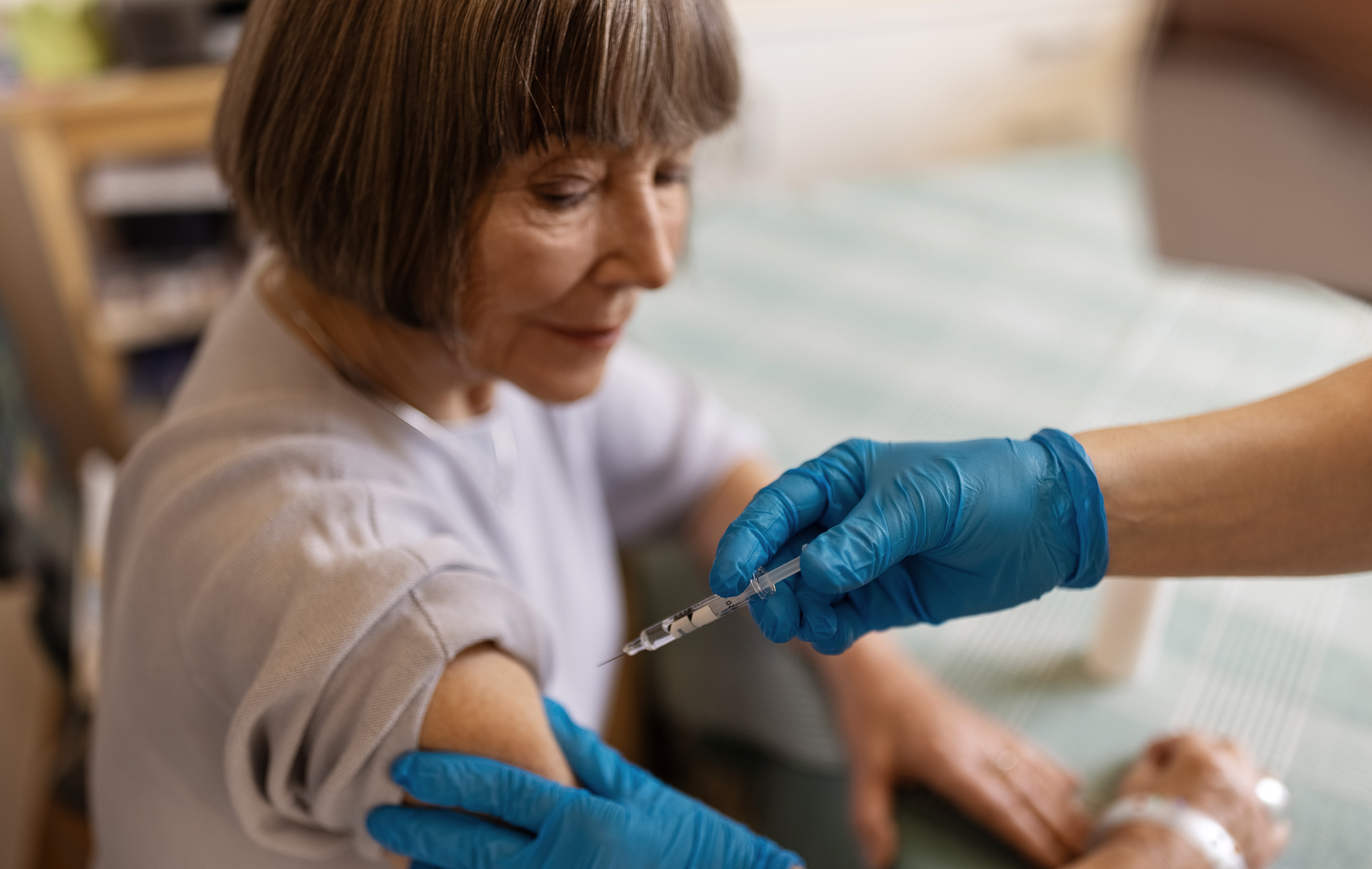 A woman receives a vaccine injection from a healthcare worker wearing blue gloves.