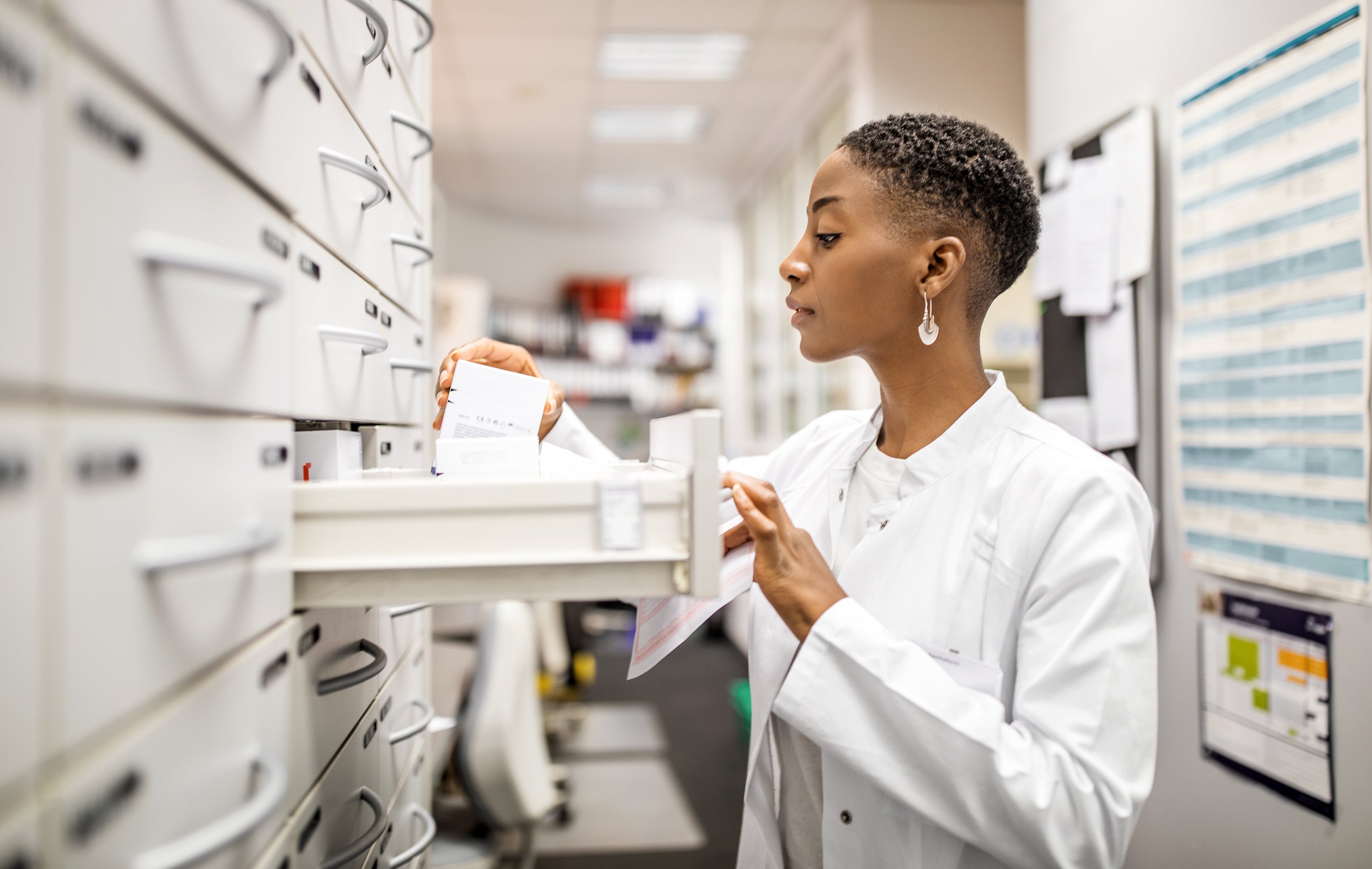 Pharmacist in white coat selects medication from a hospital pharmacy storage unit.