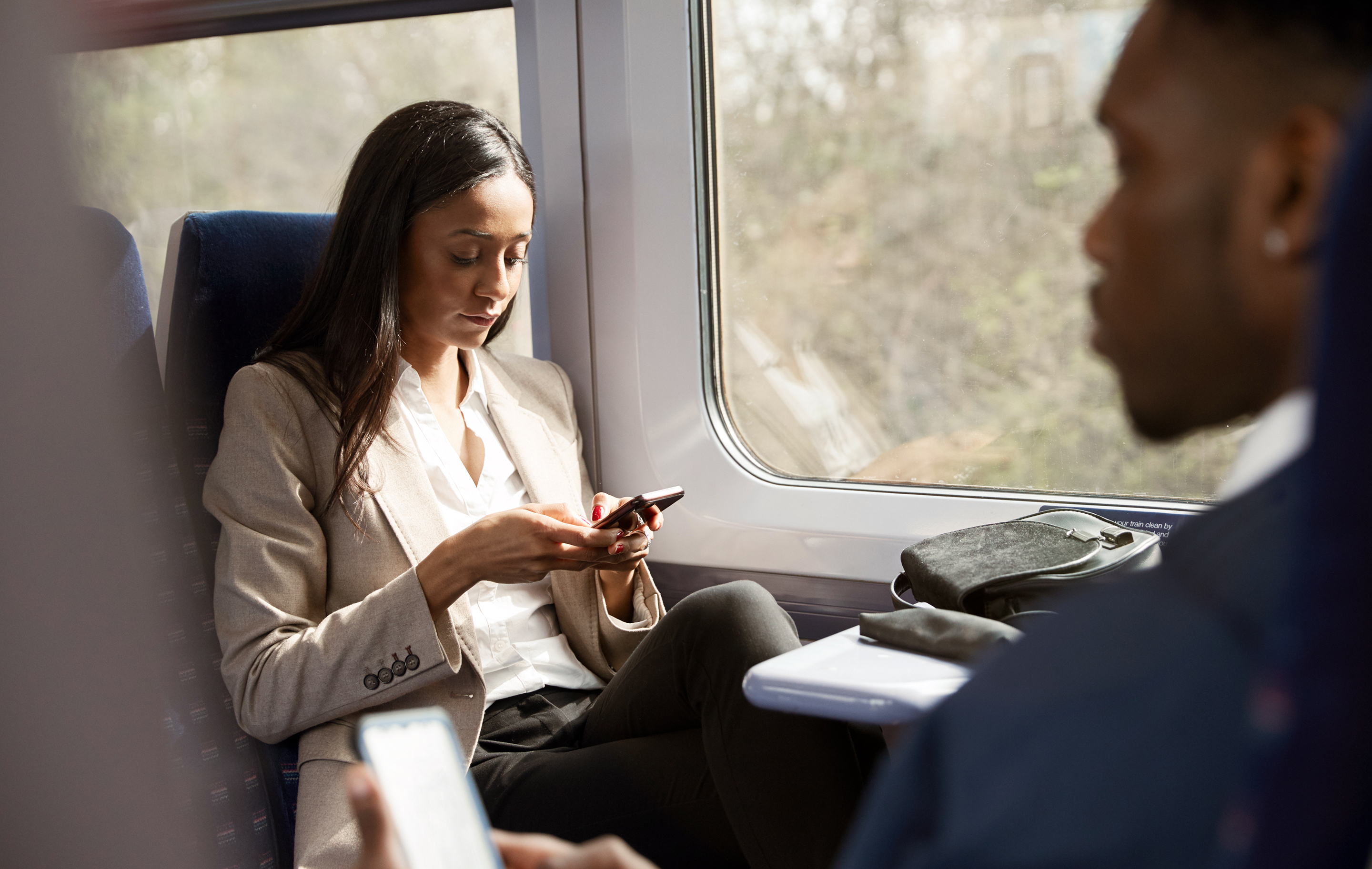 Two passengers on a train, one focused on phone the other seated nearby