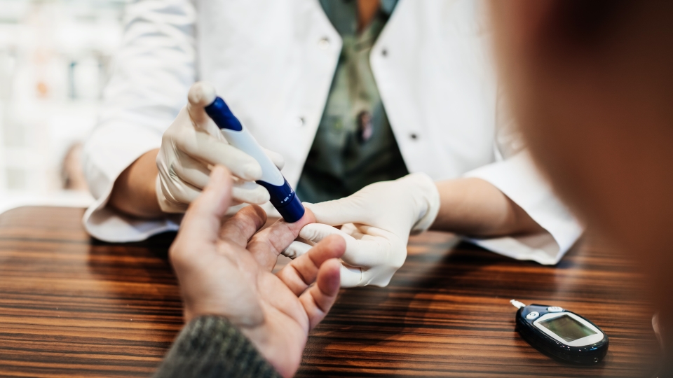Healthcare provider using glucose meter on patient's finger during blood sugar test.