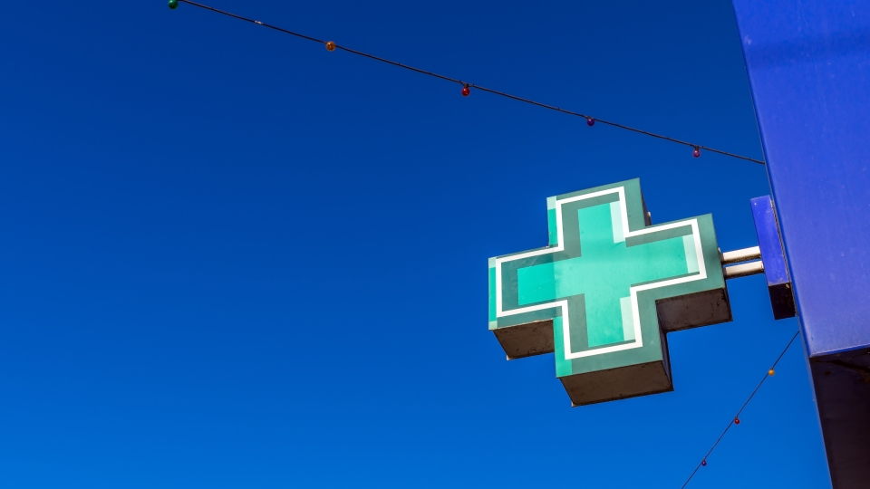 Teal plus sign logo against a clear blue sky with thin wires overhead.