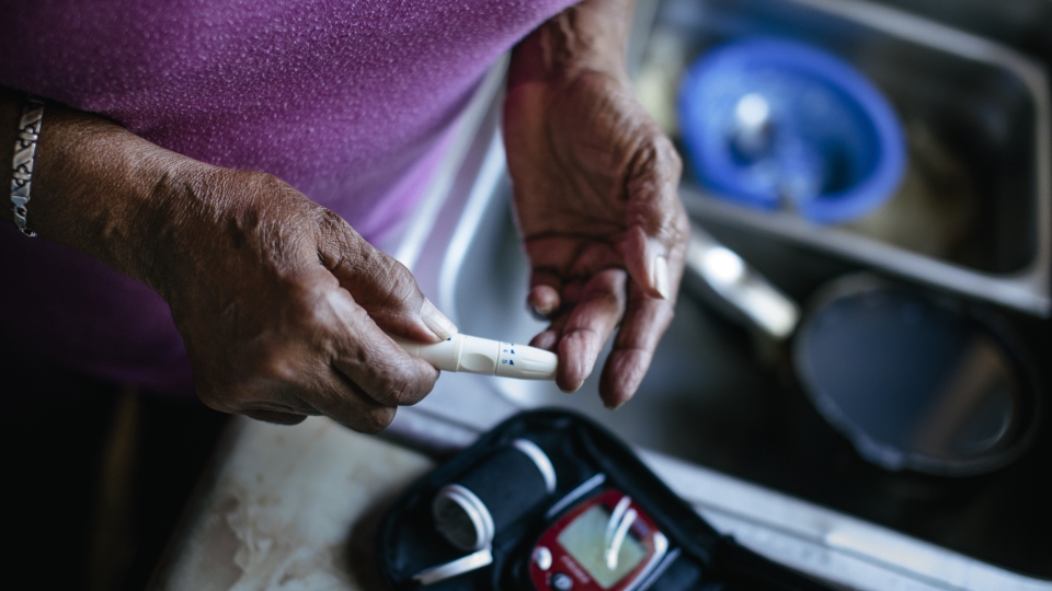 Person holding glucose test stick near sink with blood sugar meter nearby