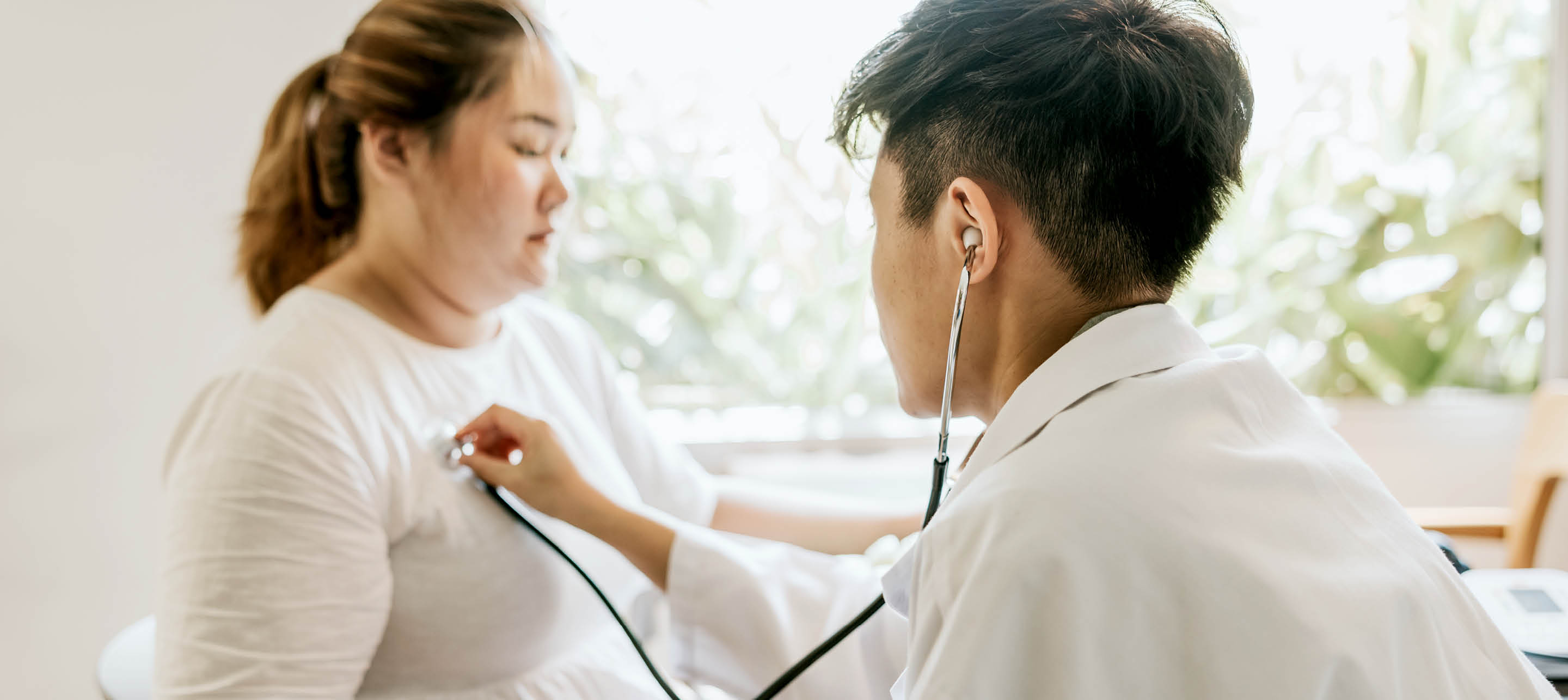 Healthcare professional uses stethoscope to listen to patient's chest in bright, calm clinic setting.