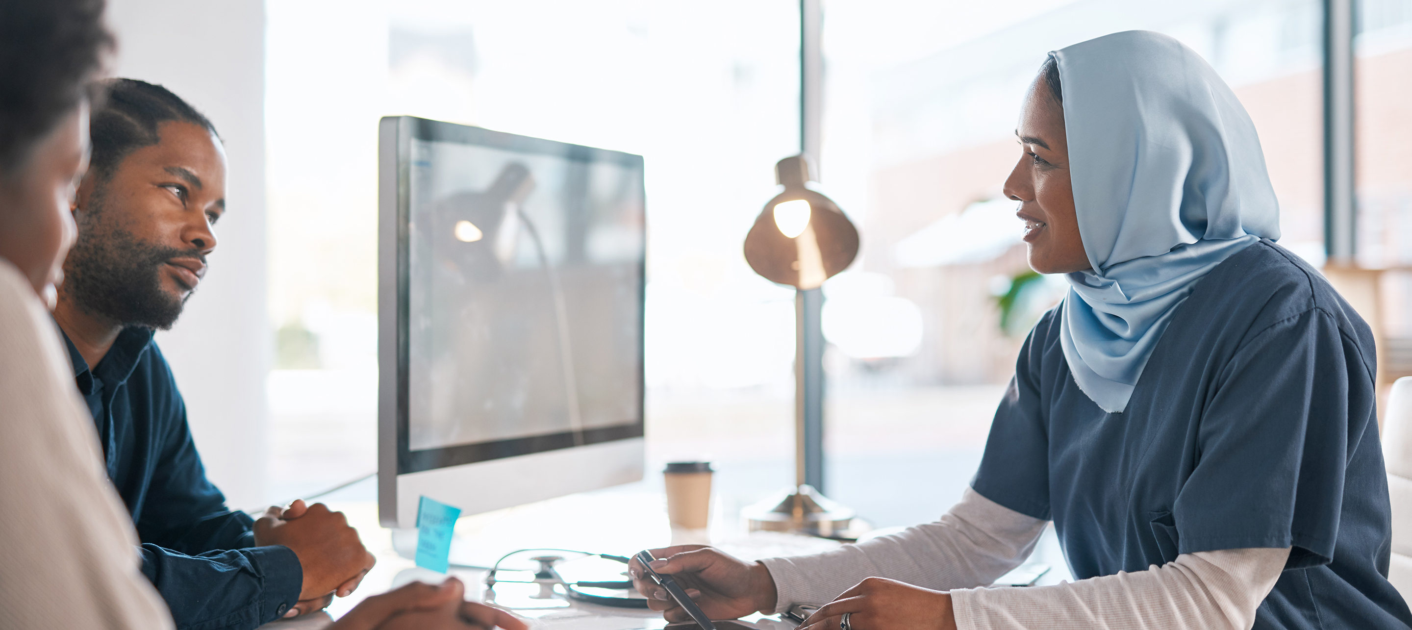 Two individuals with a healthcare provider at desk in office