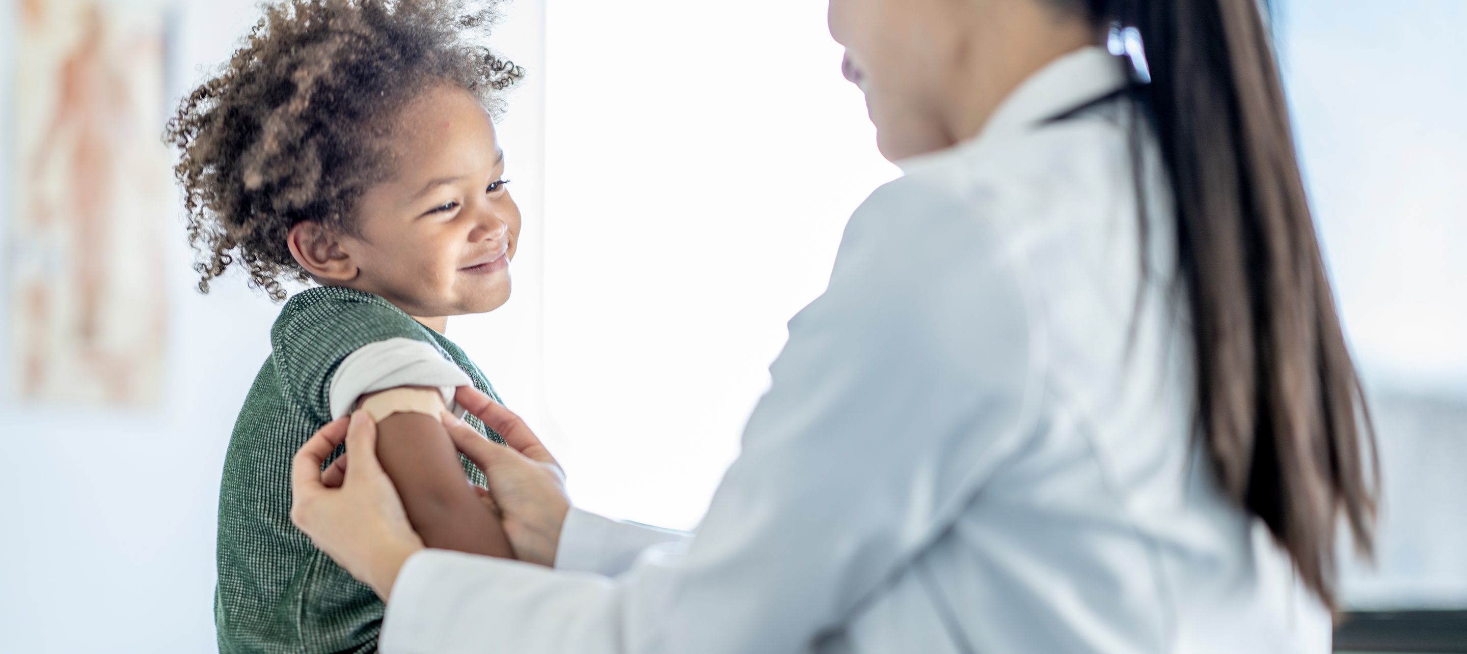 A young child smiles as a healthcare provider gently holds their arm during a medical visit.