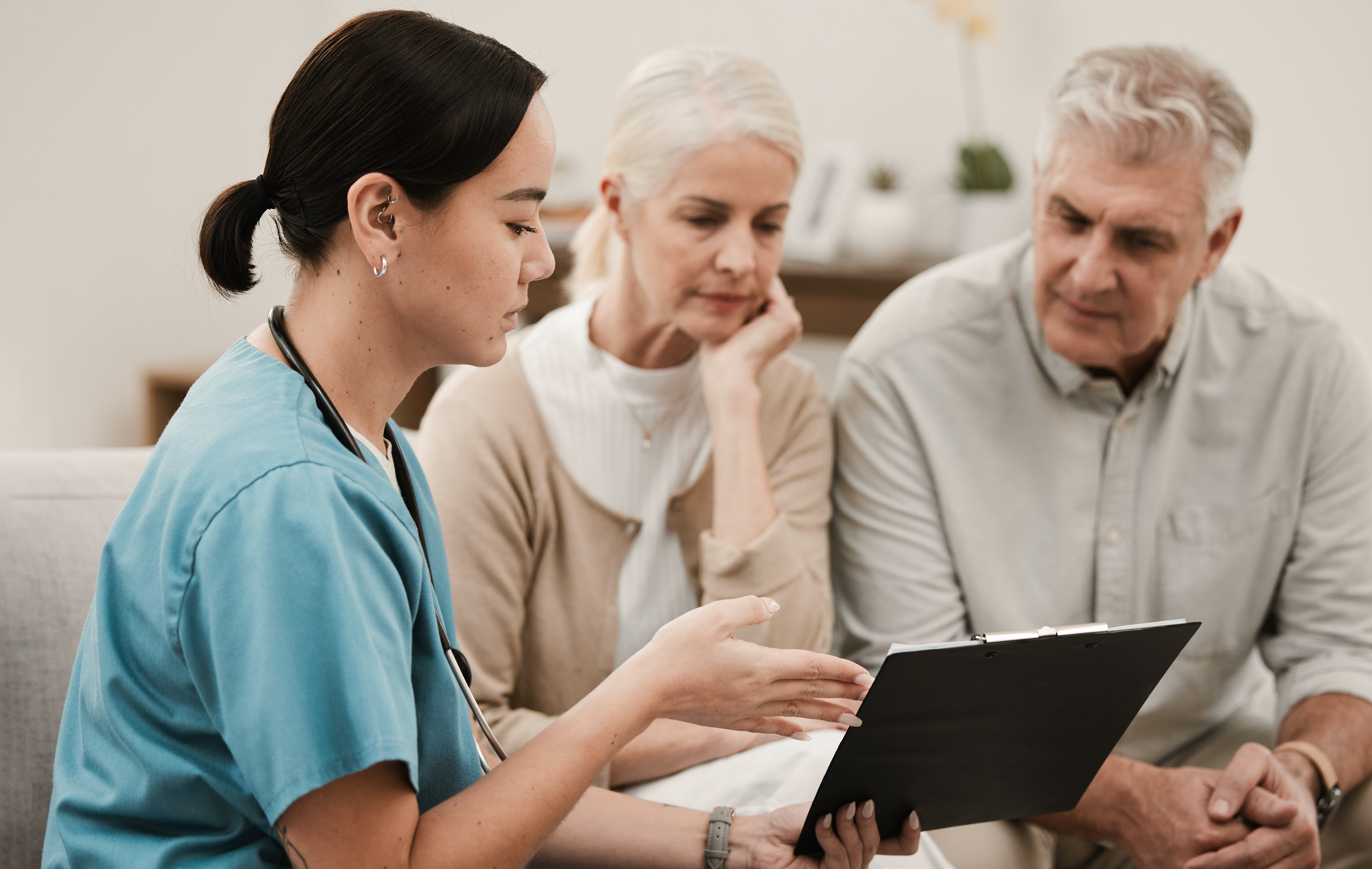 Healthcare provider explains medical information to elderly couple seated together in softly lit room.