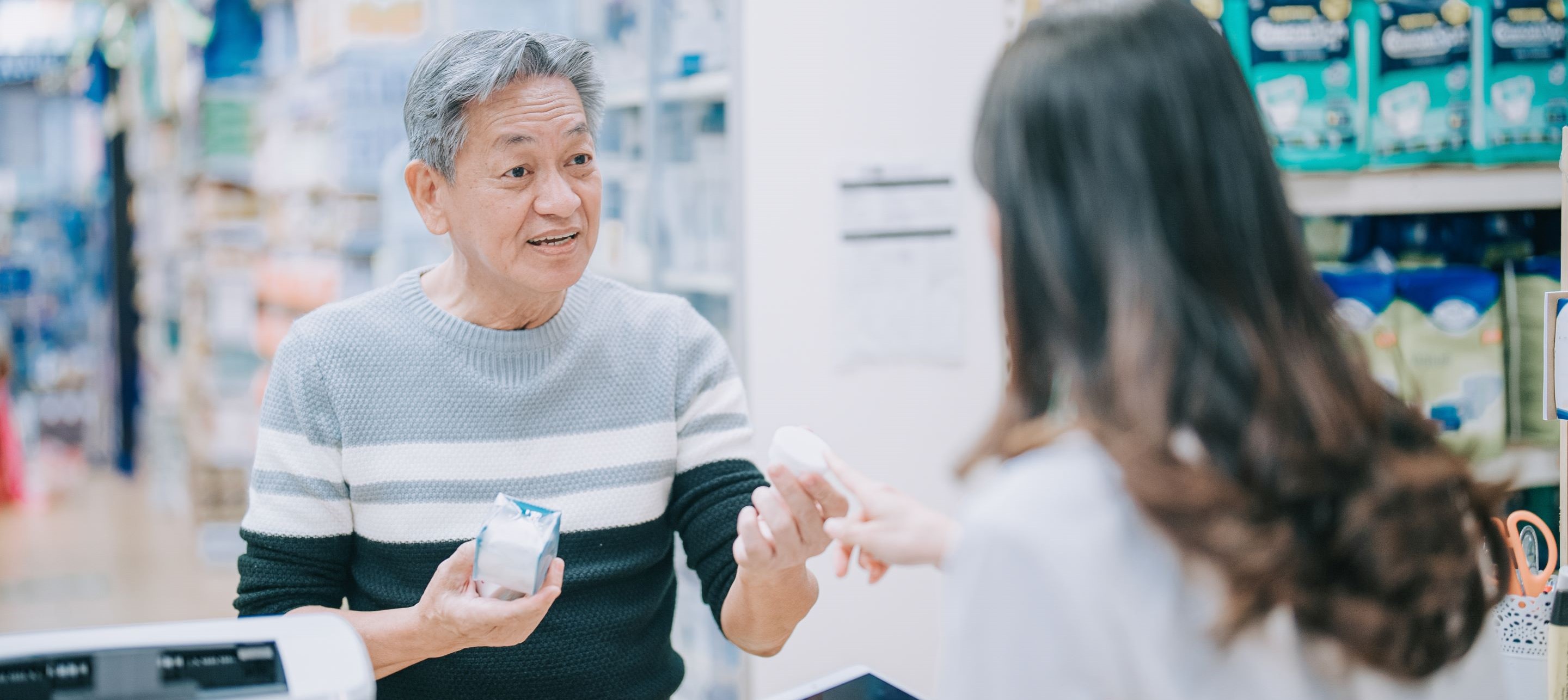 Man smiles while holding a medication, engaging with a pharmacist