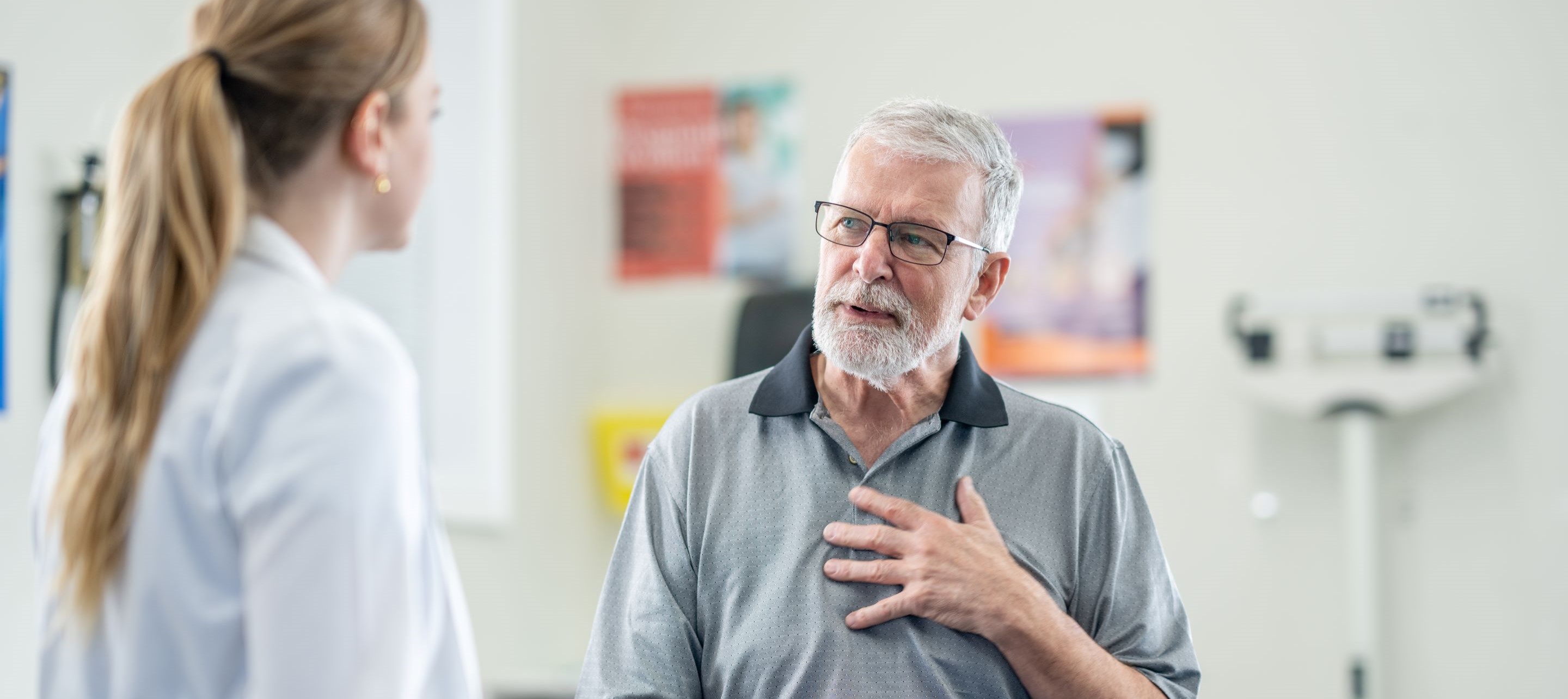 Man in medical office holding chest as he speaks with a doctor.