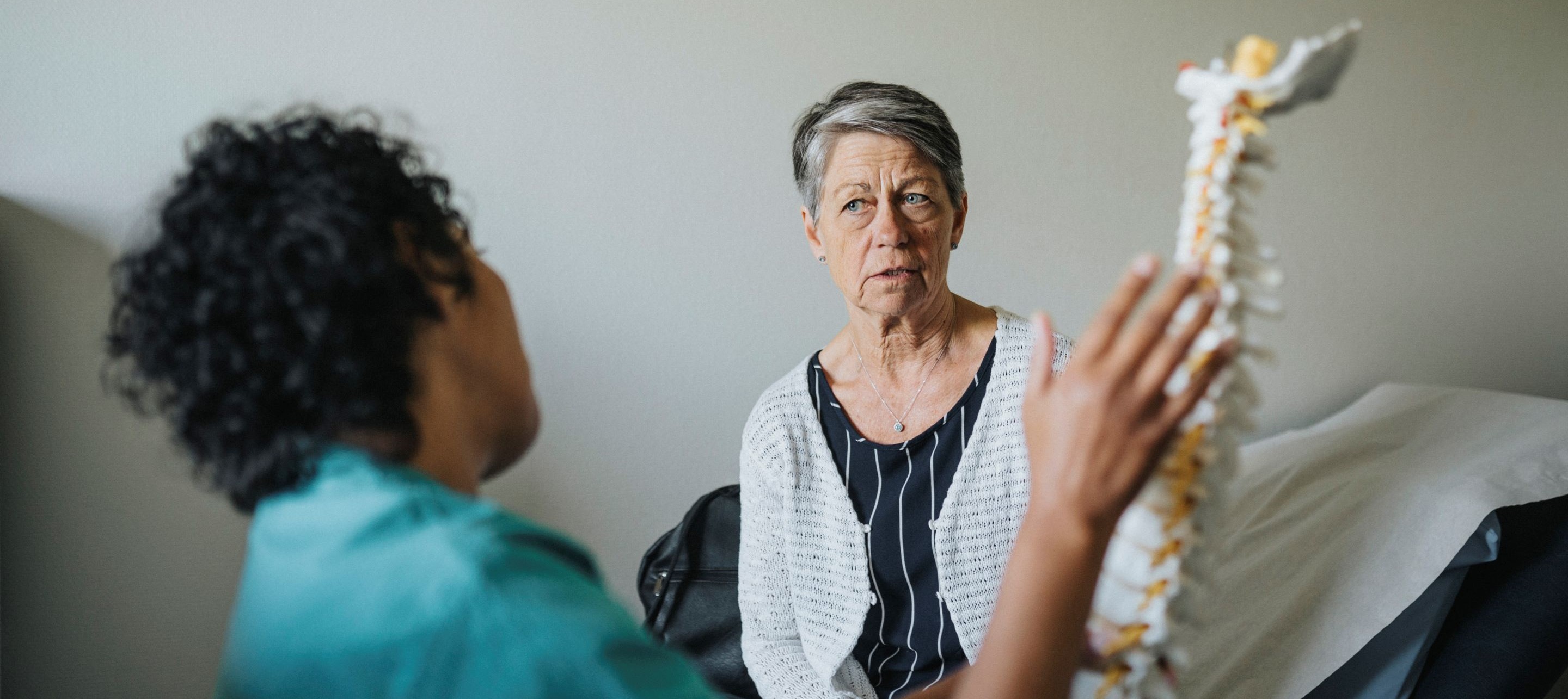 Healthcare professional shows spine model to patient during consultation in clinical setting.