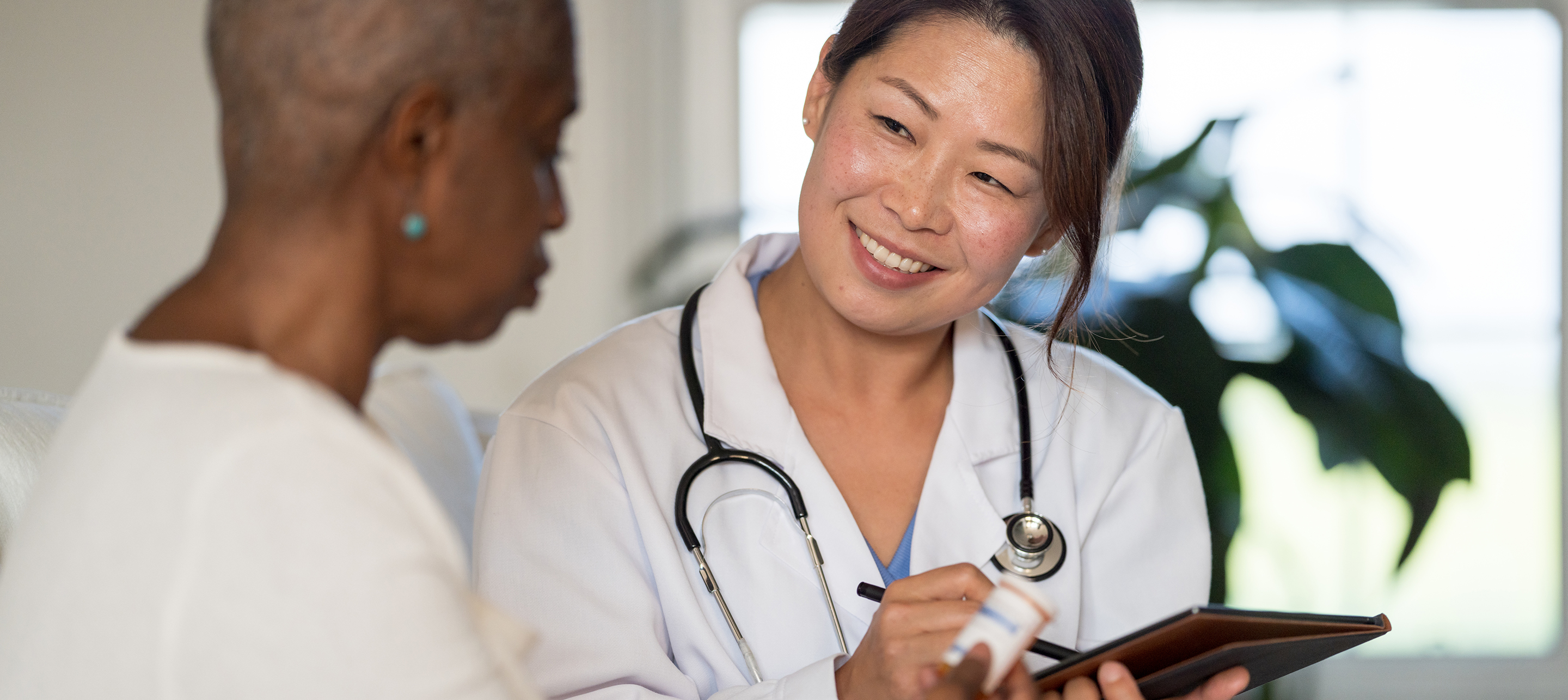 Smiling woman doctor with stethoscope around neck, holding tablet talking to woman