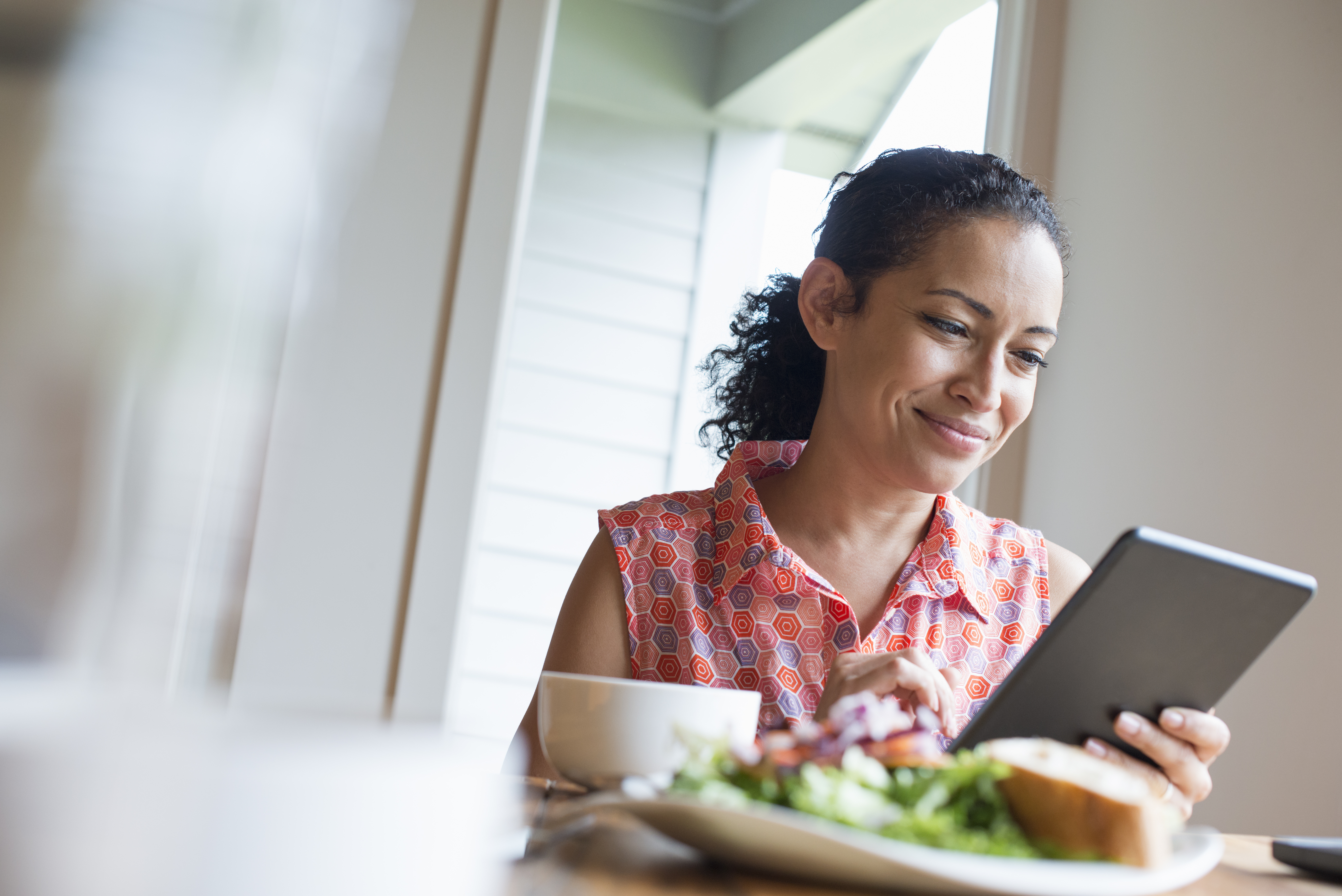 Smiling woman reading tablet at table with plate of food
