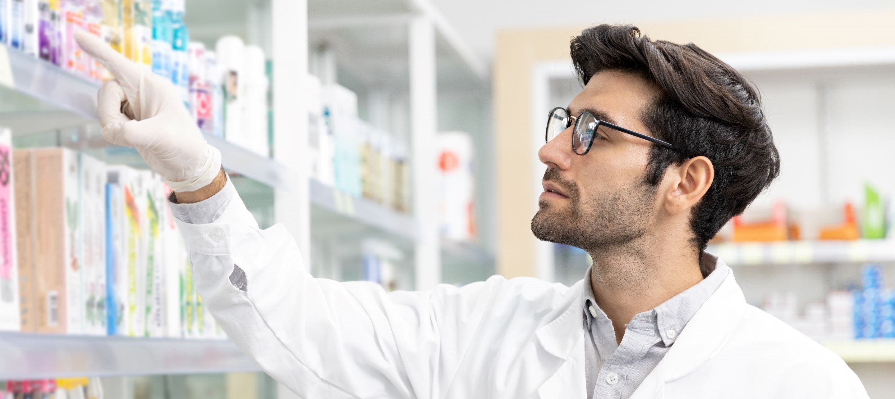 A pharmacist in a white pointing at items on a shelf.