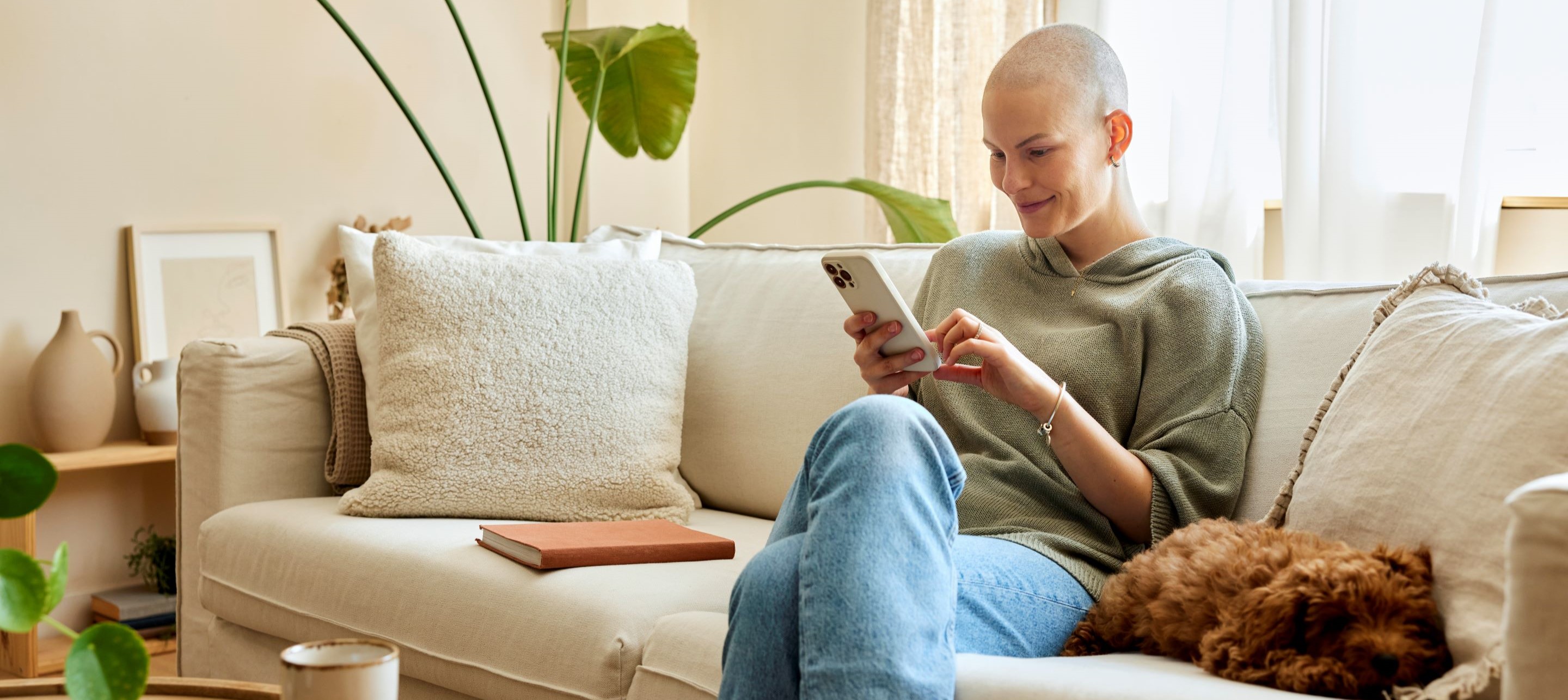 Woman sitting on couch looking at phone with smile, dog laying next to her.