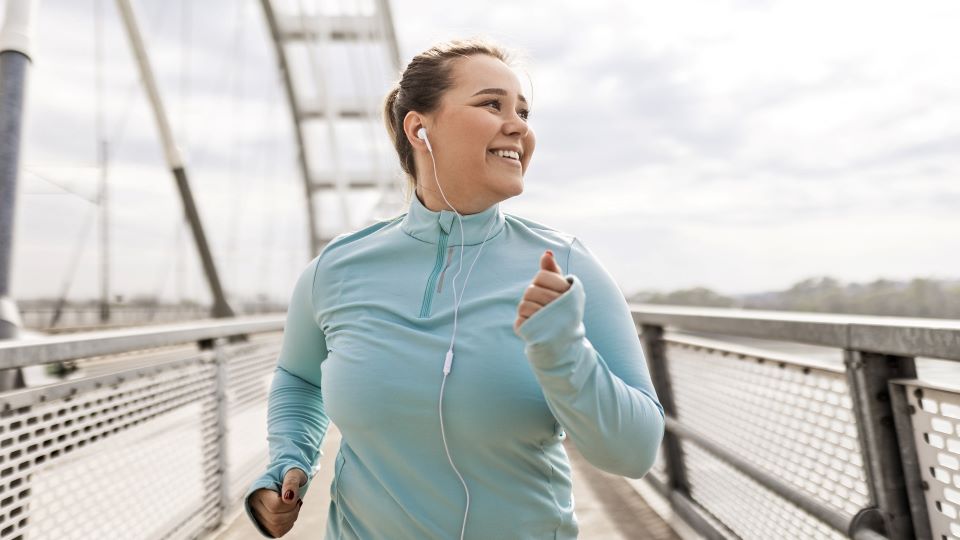Woman jogging on bridge with a blue jacket and white earphones.