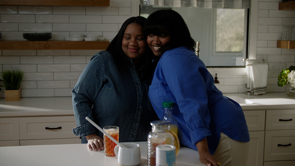 Two women smile, leaning on counter