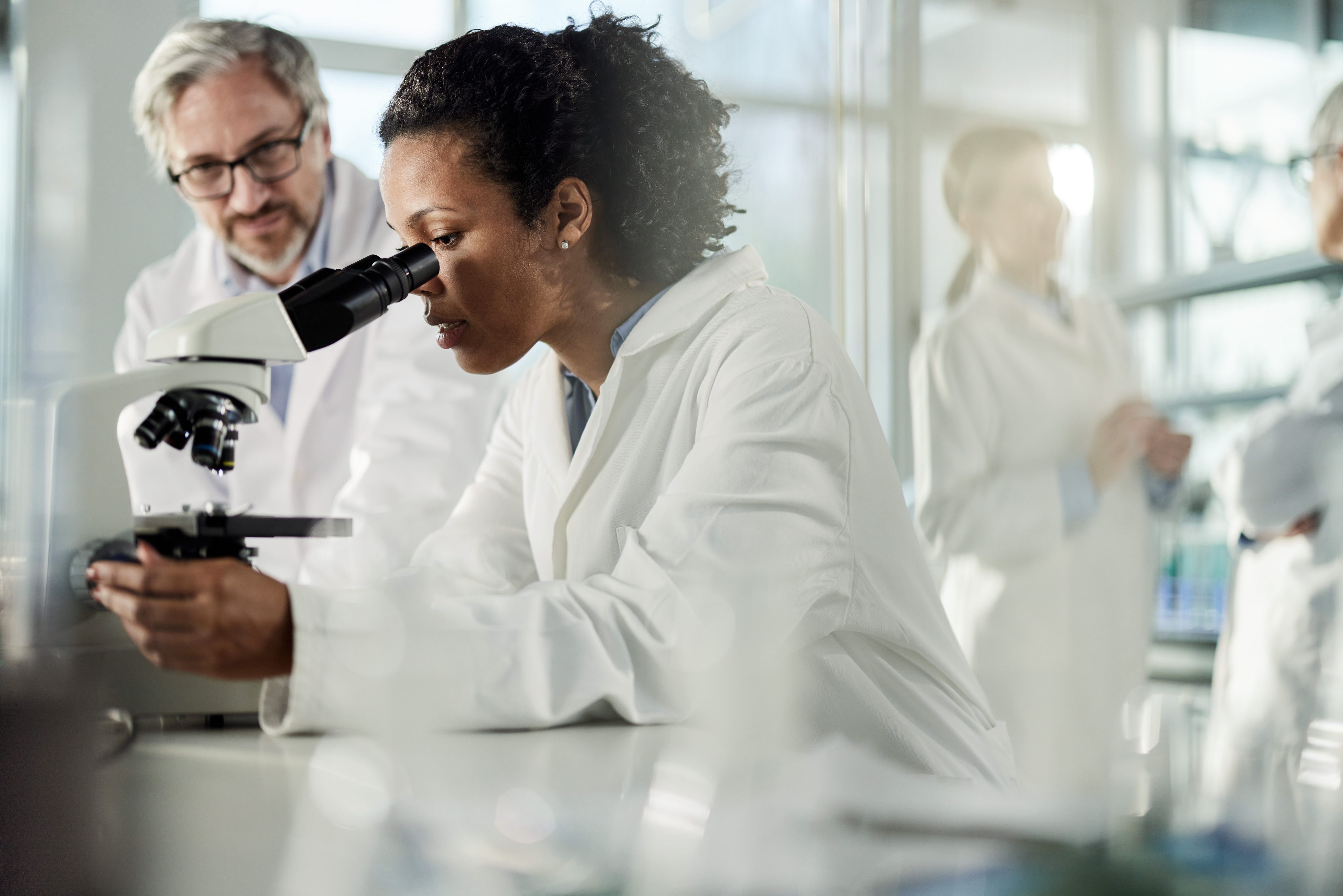 female doctor sitting looking into microscope with male doctor sitting