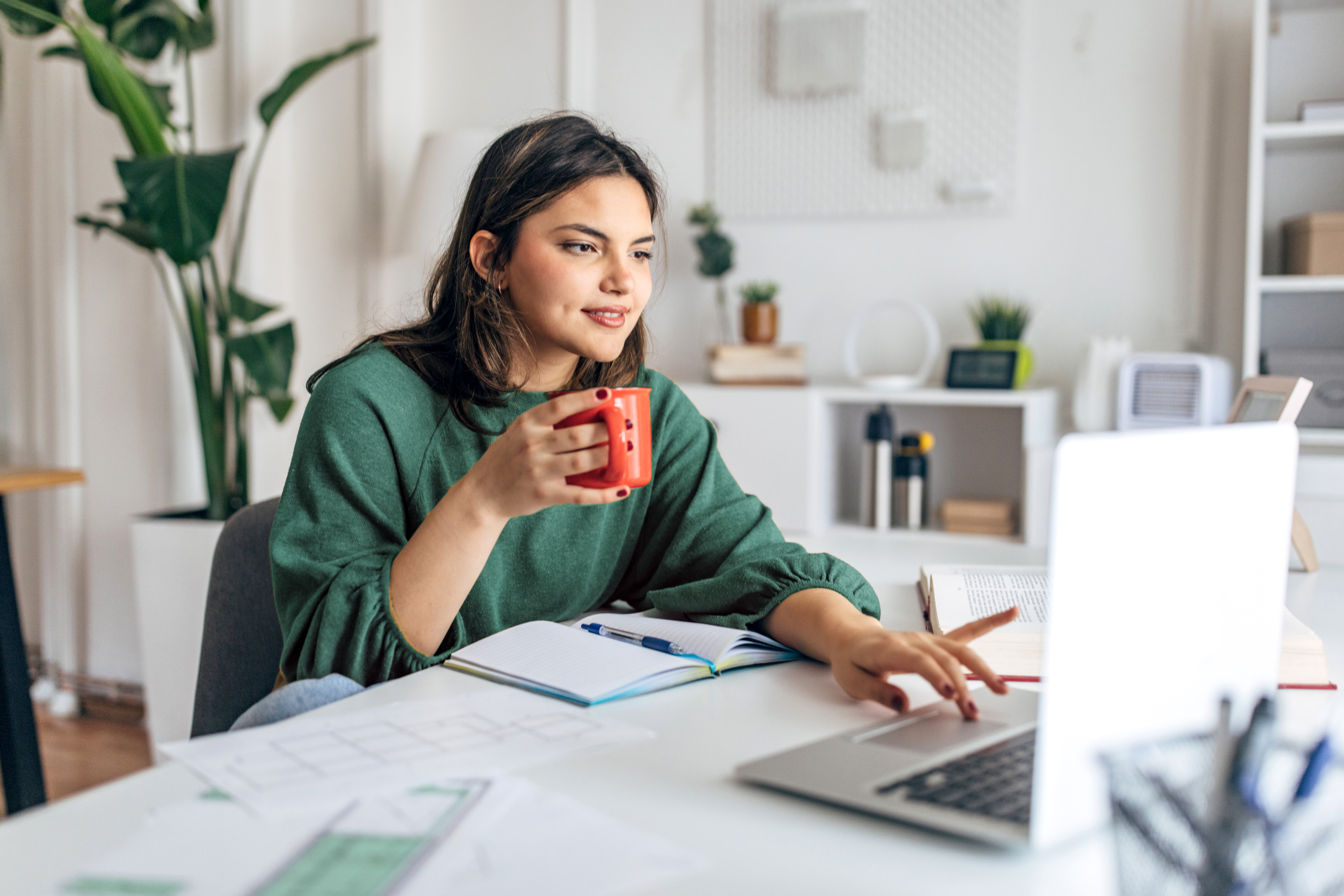 young woman holding mug viewing laptop