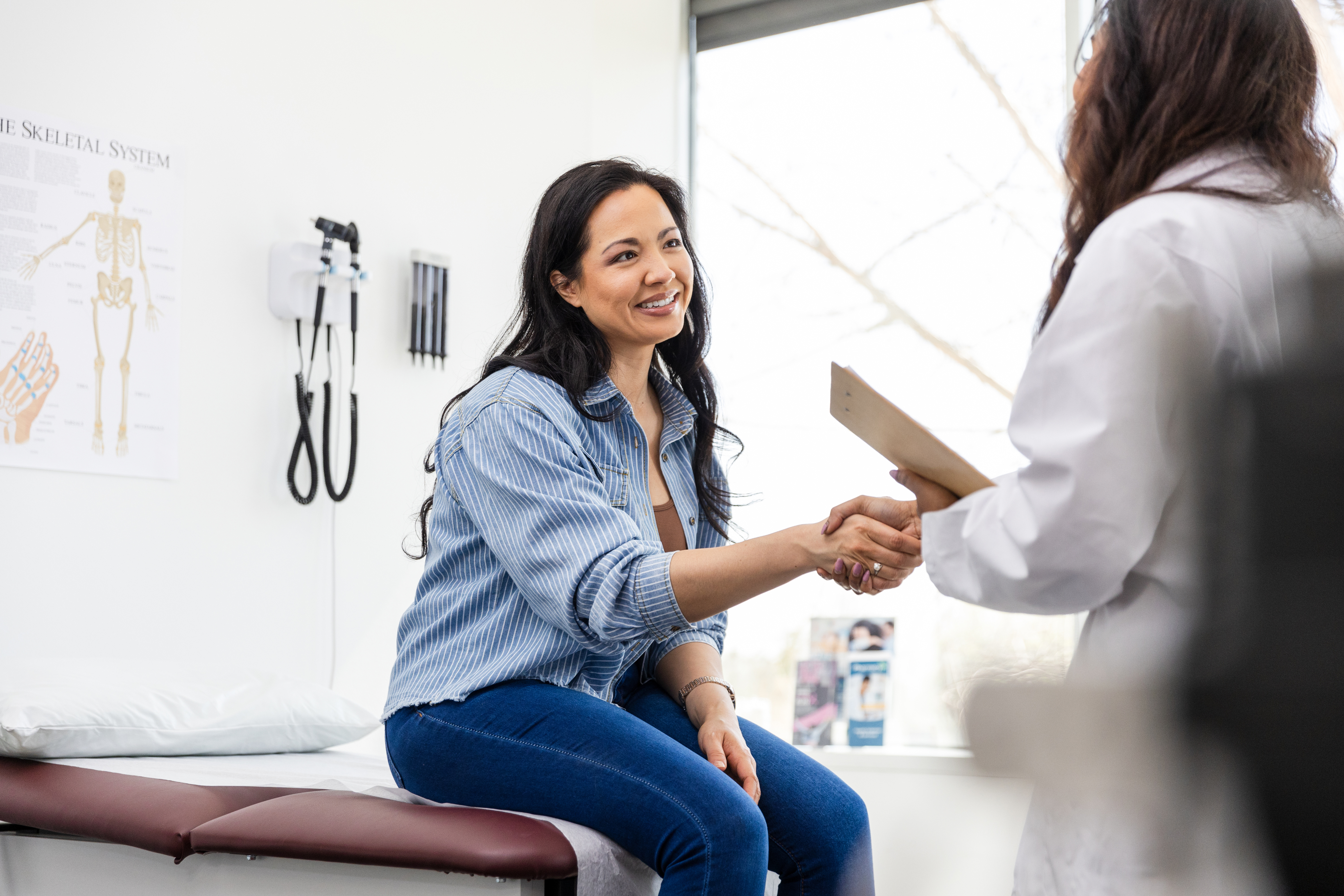 Woman sitting on exam table shaking hands with female doctor