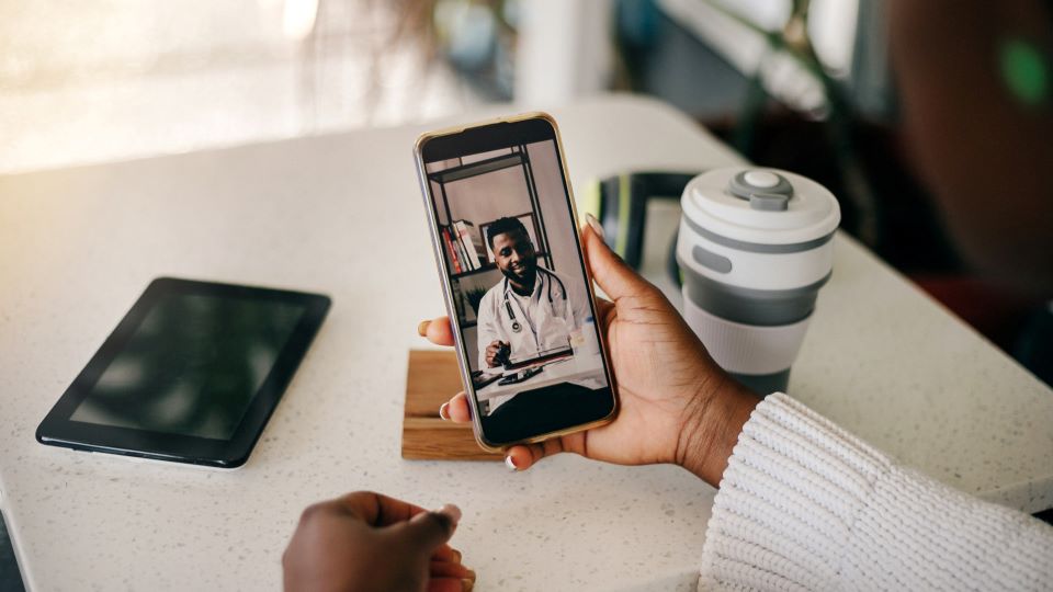 Hand holding smartphone displaying a doctor on a video call