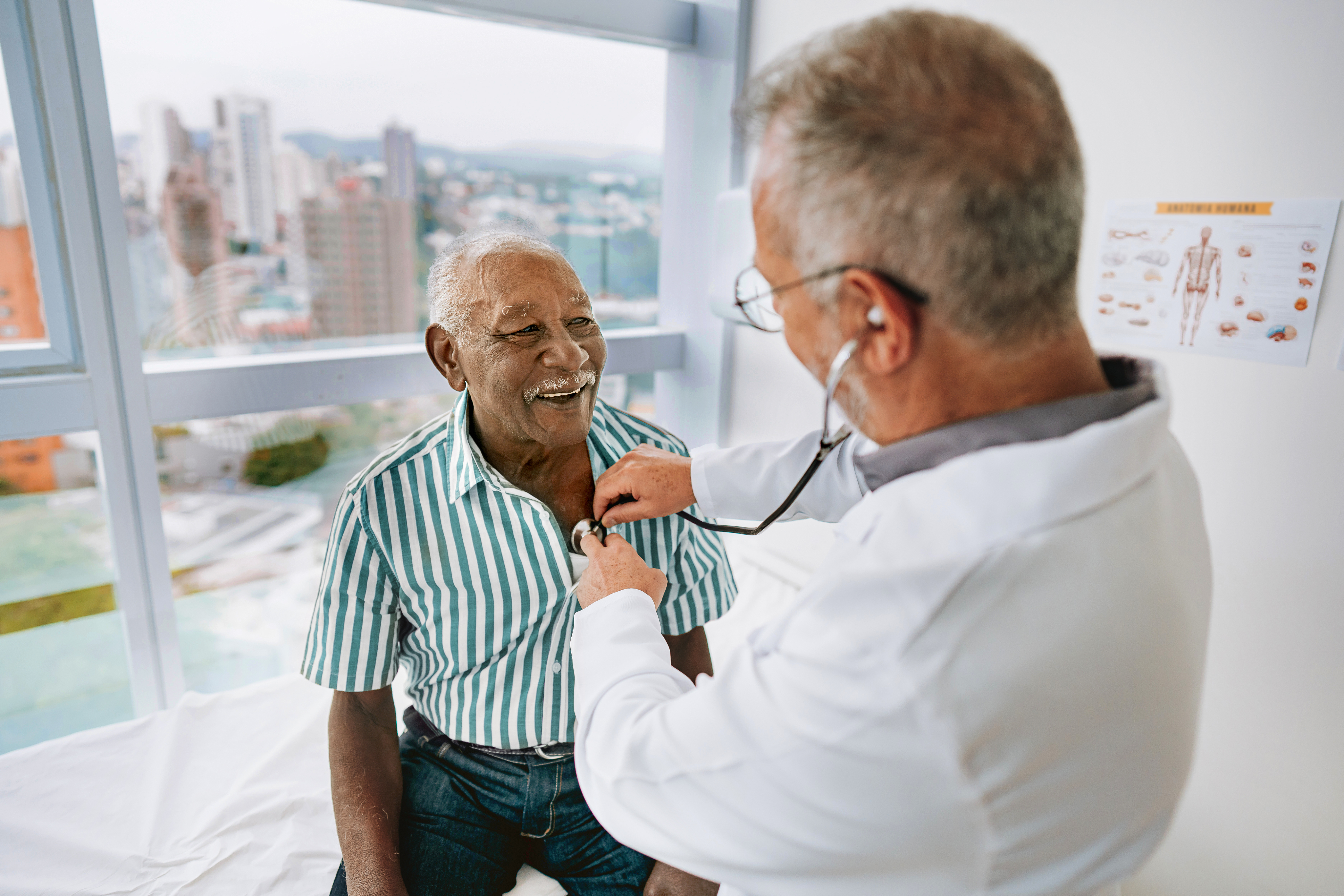 Doctor examining older patient with stethoscope sitting on exam table