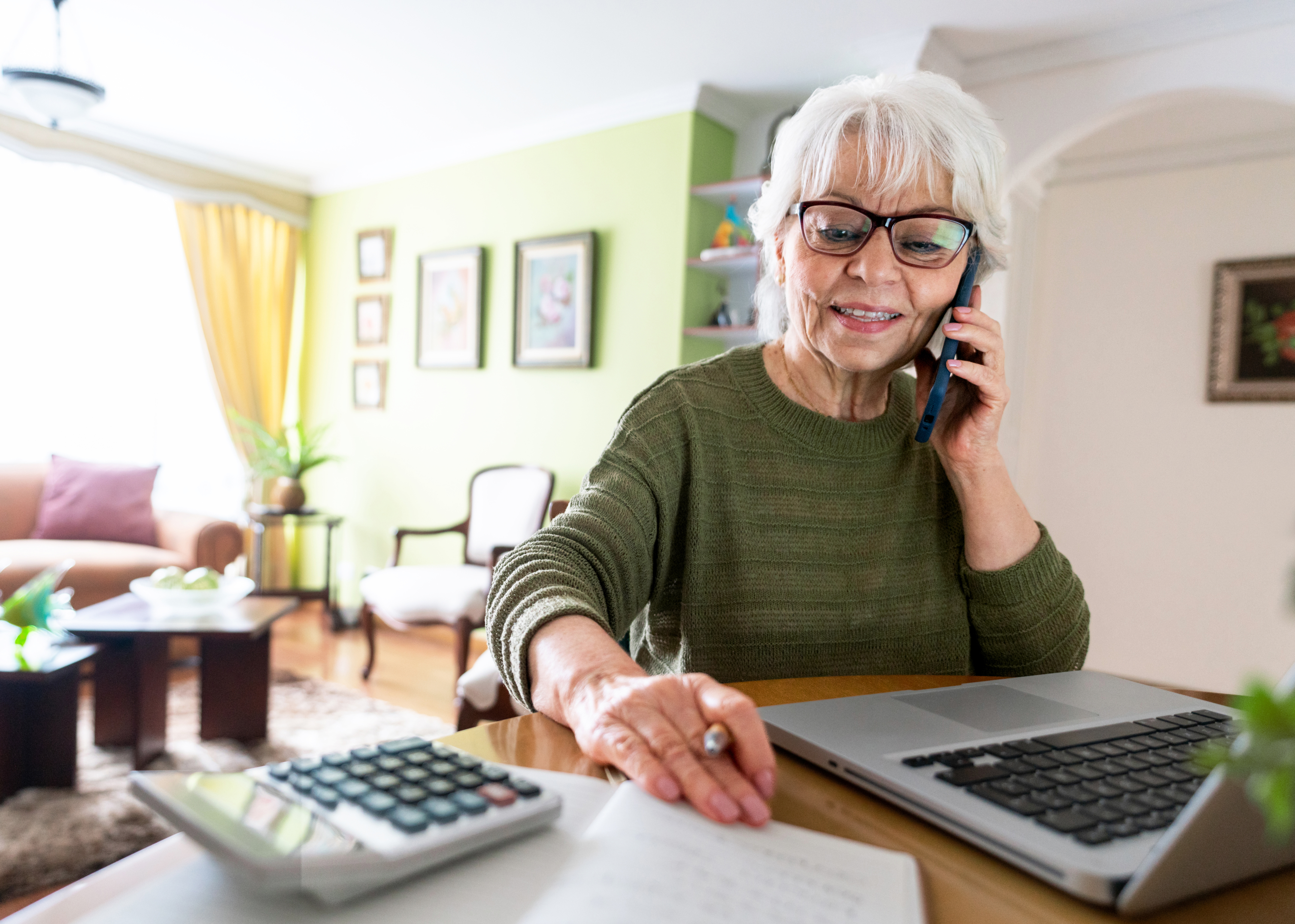 mature woman sitting at table holding the phone with laptop
