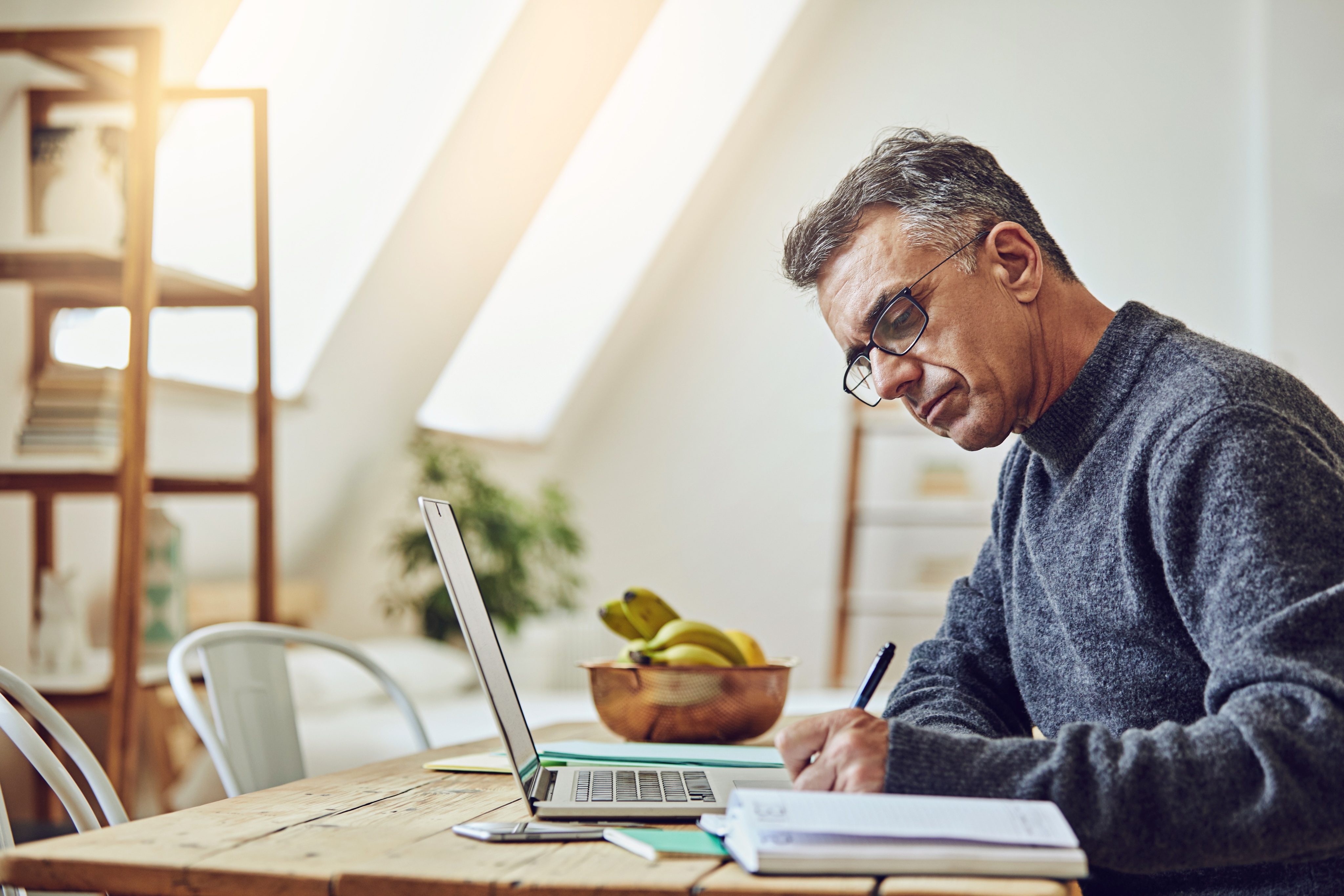 man at desk writing in front of laptop