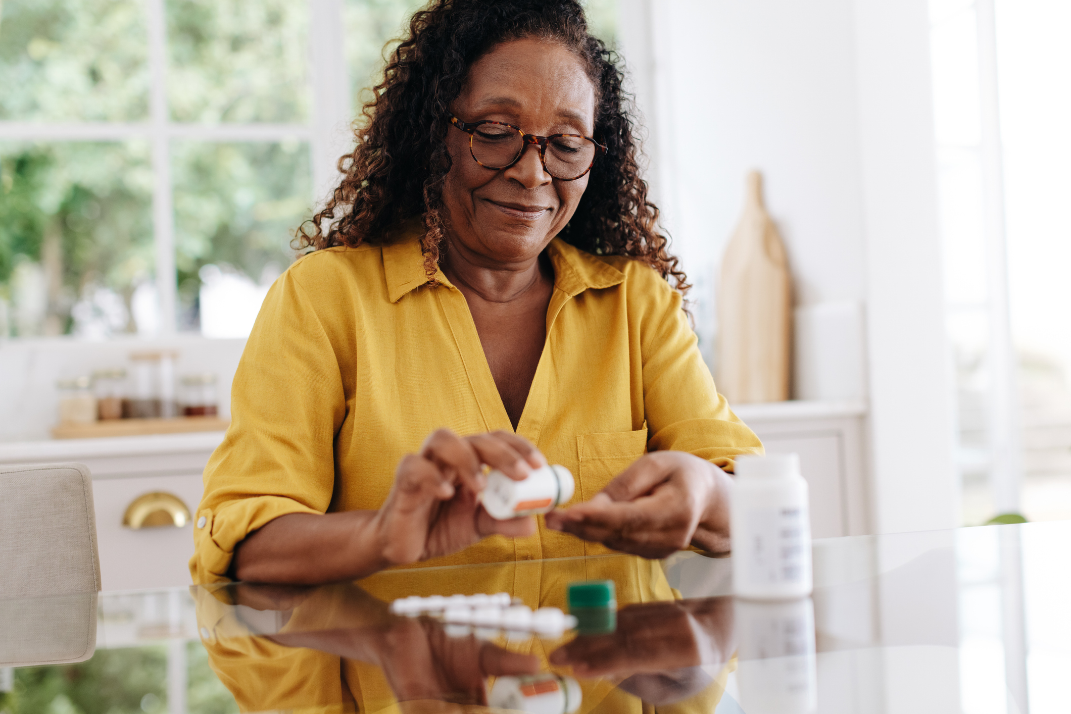 Woman at home opening a bottle of prescription medications with a neutral expression