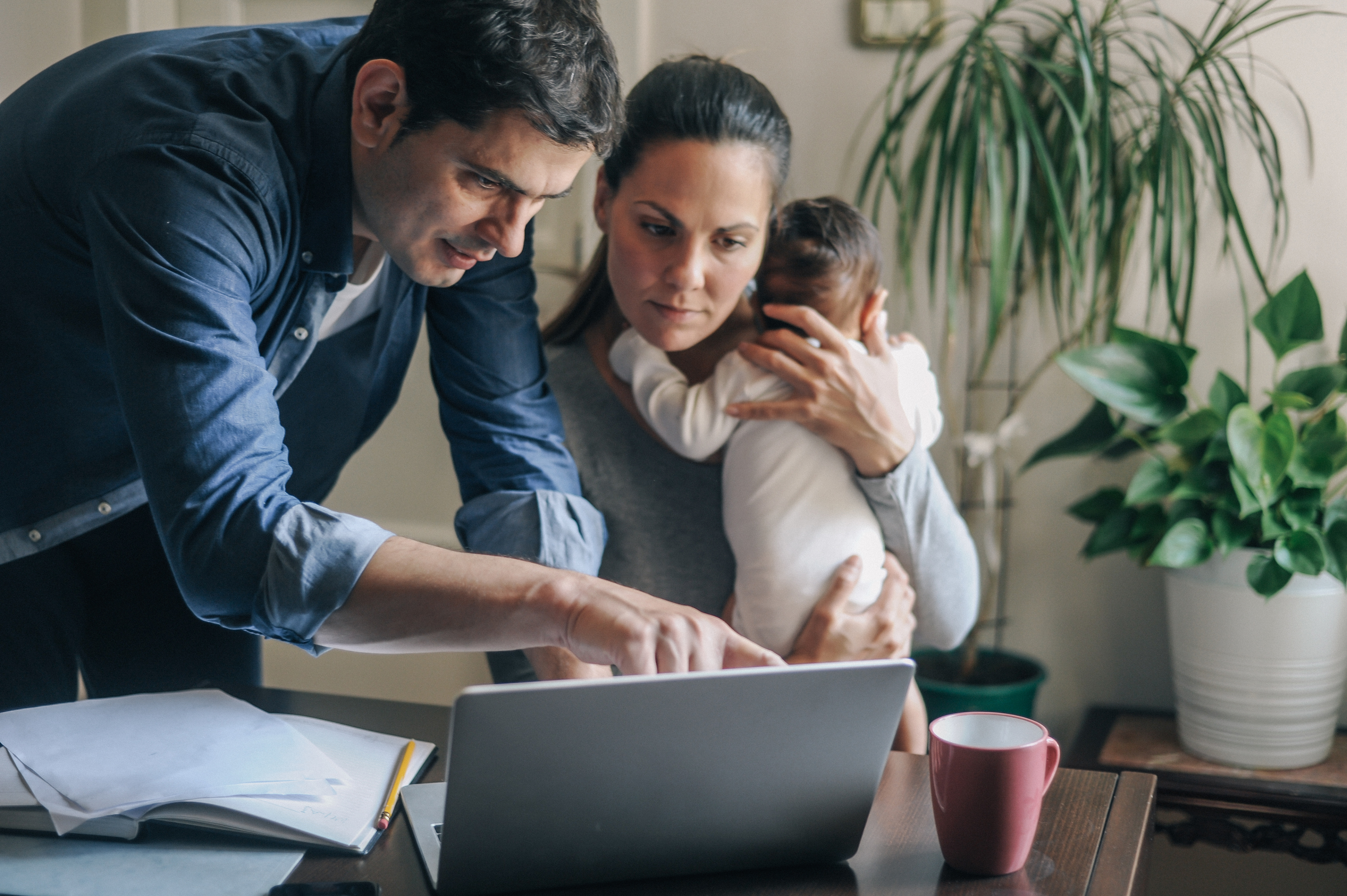 Man with woman holding infant looking at laptop