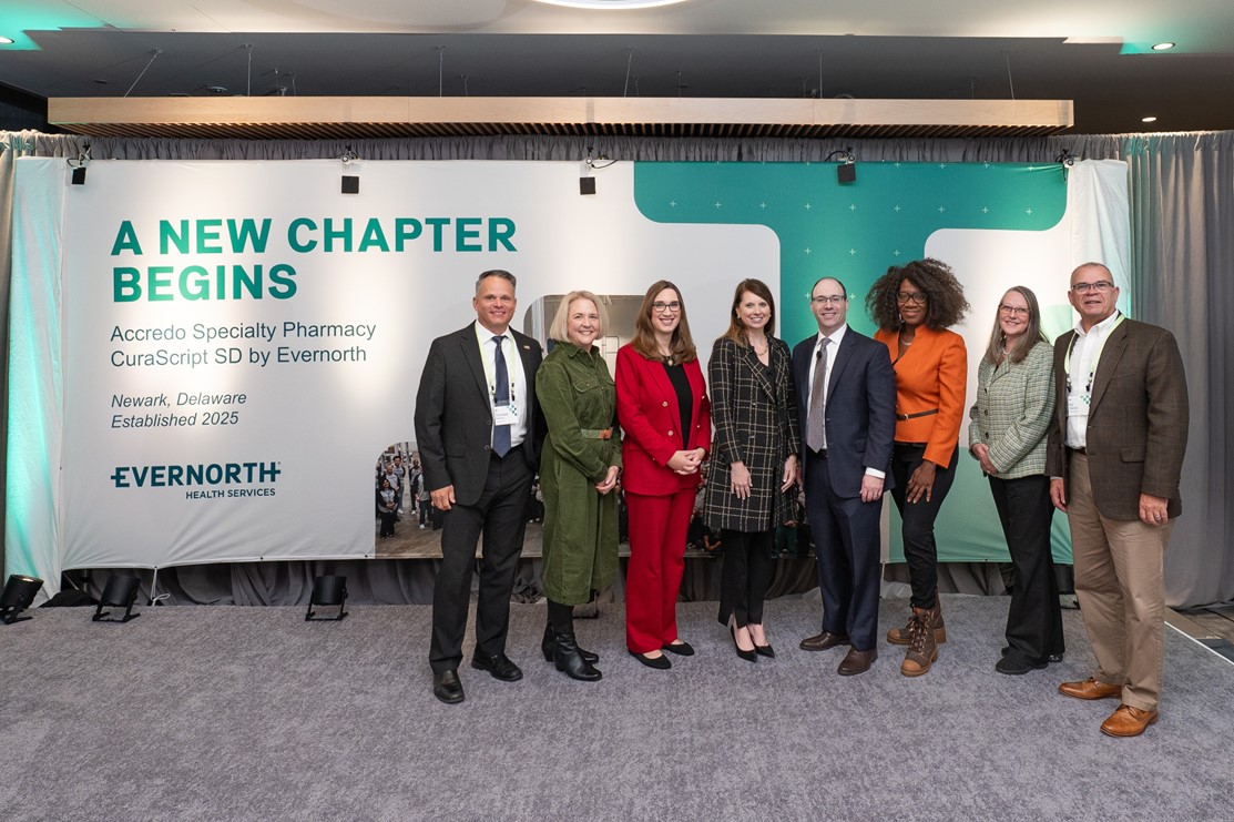 Eight Evernorth executives/employees pose for a group photo in front of a decorative banner celebrating the launch of a new specialty facility in Newark, DE.